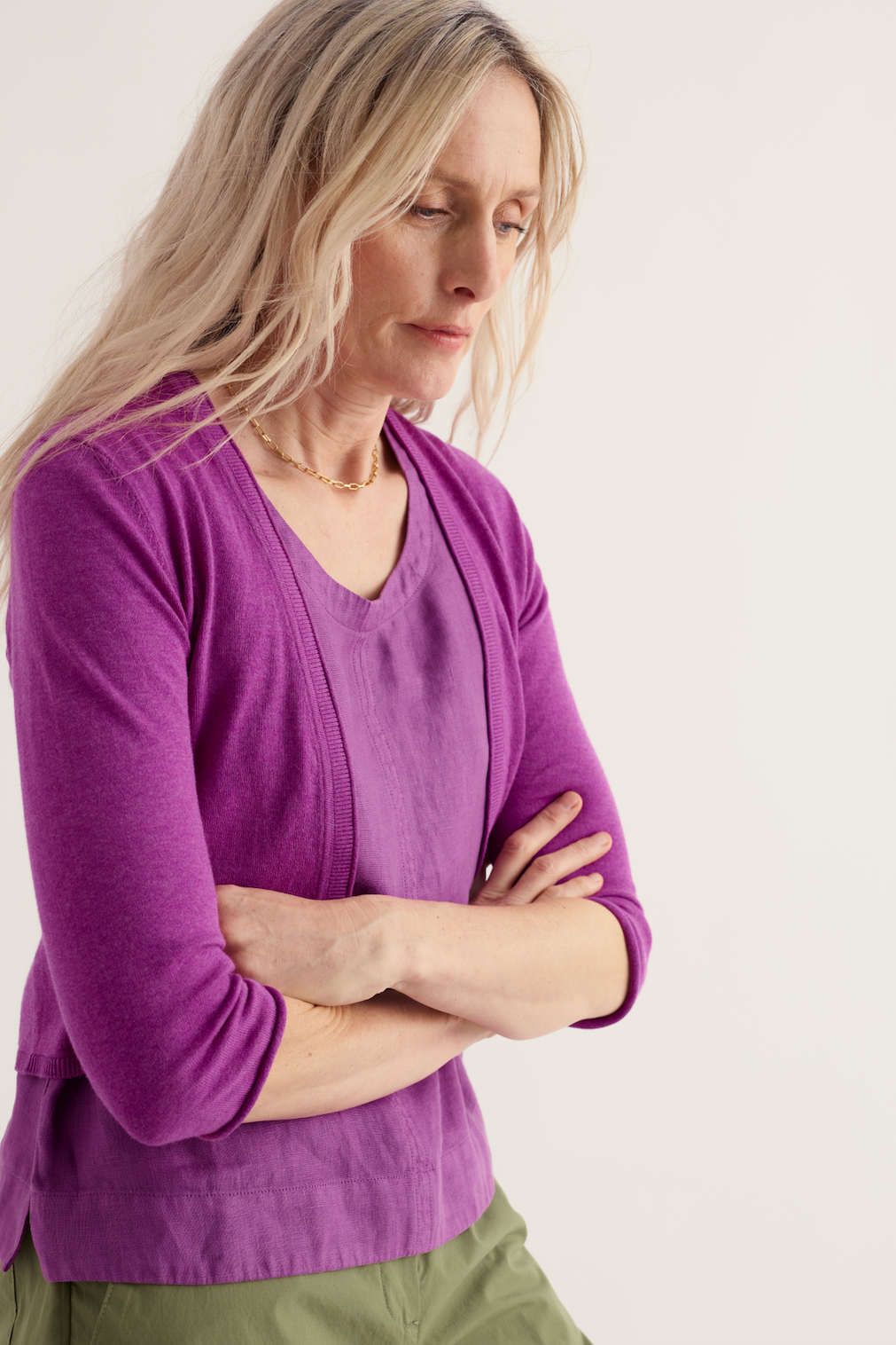 A woman wearing a vibrant purple Seasalt organic cotton cardigan with arms crossed against a neutral background.