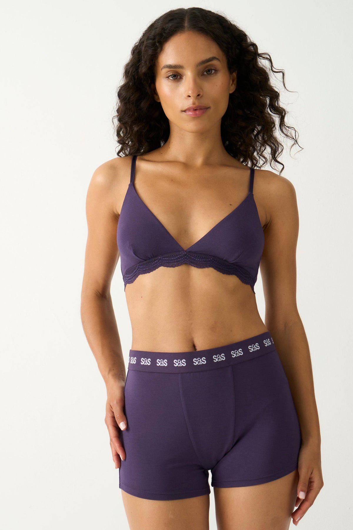 A model posing in a purple Stripe & Stare bralette and matching women's boxer underwear set.