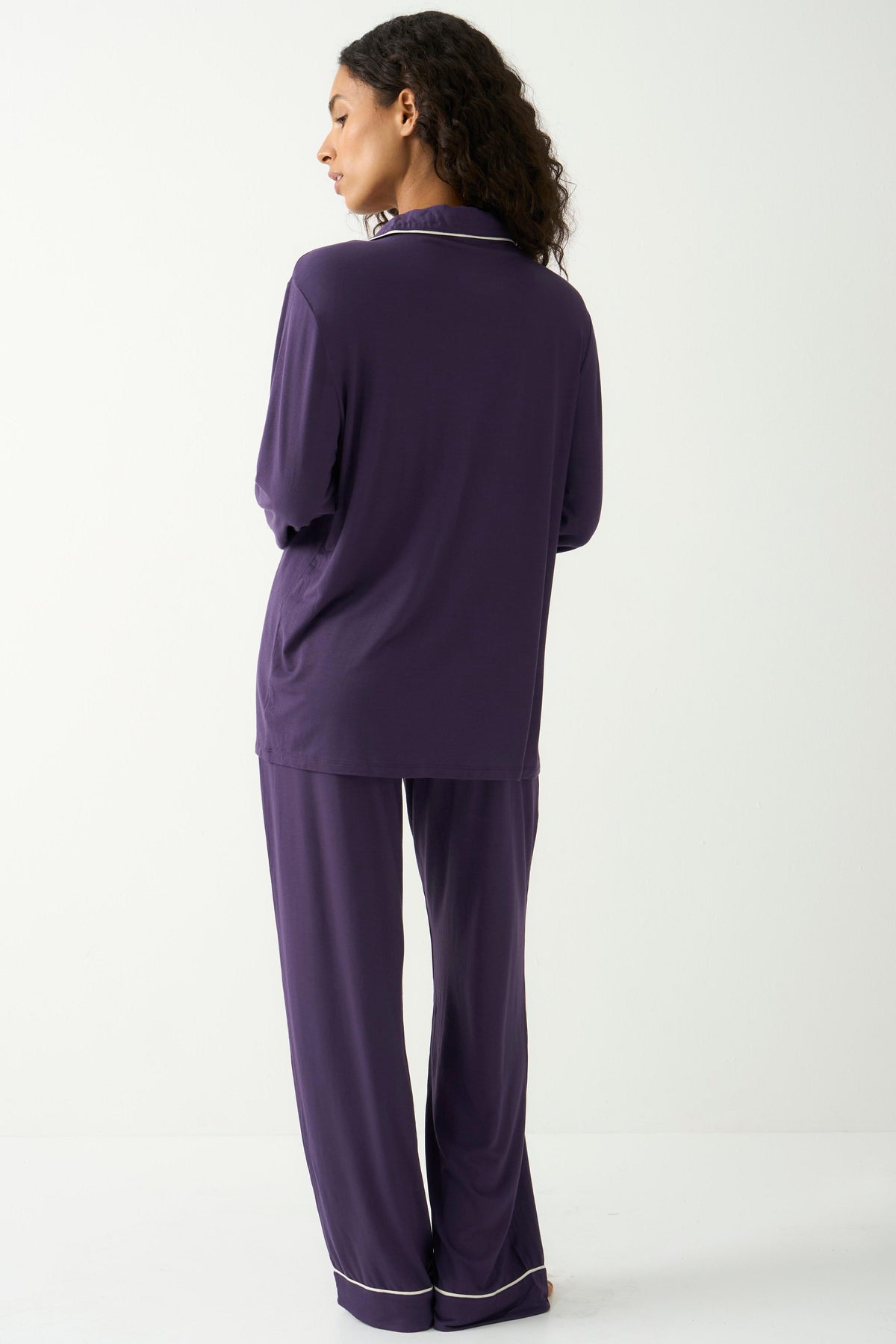 Woman standing in dark purple luxury tencel pyjamas against a white background