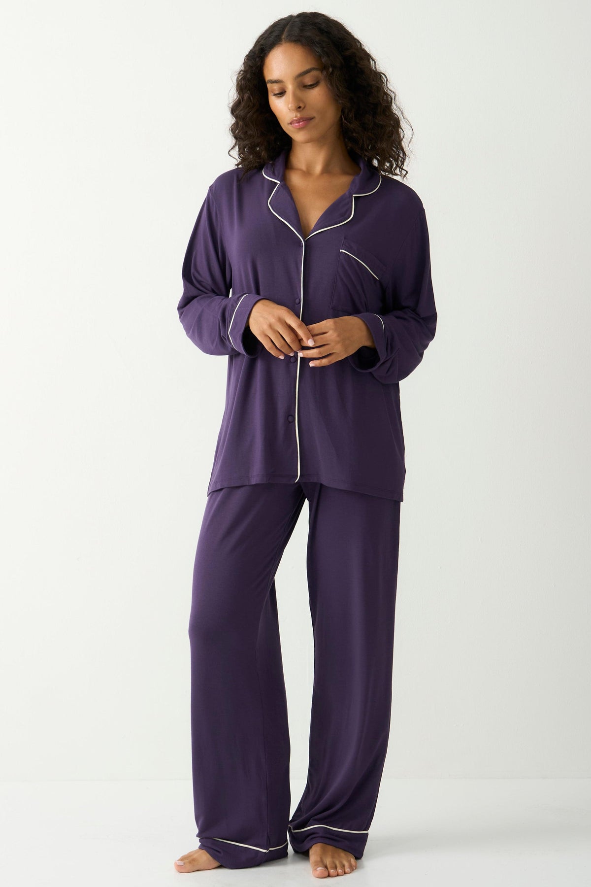 A woman modeling soft purple Tencel pyjamas with white piping detail against a white background.