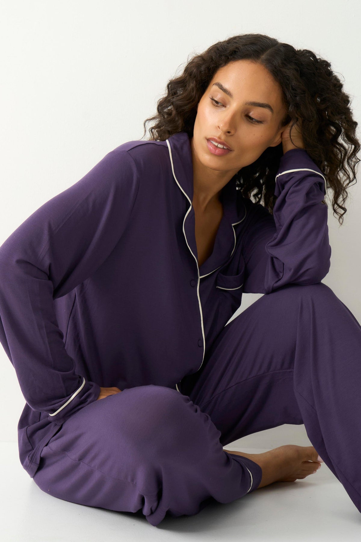Woman with curly hair sitting down wearing a luxury purple tencel pyjama set