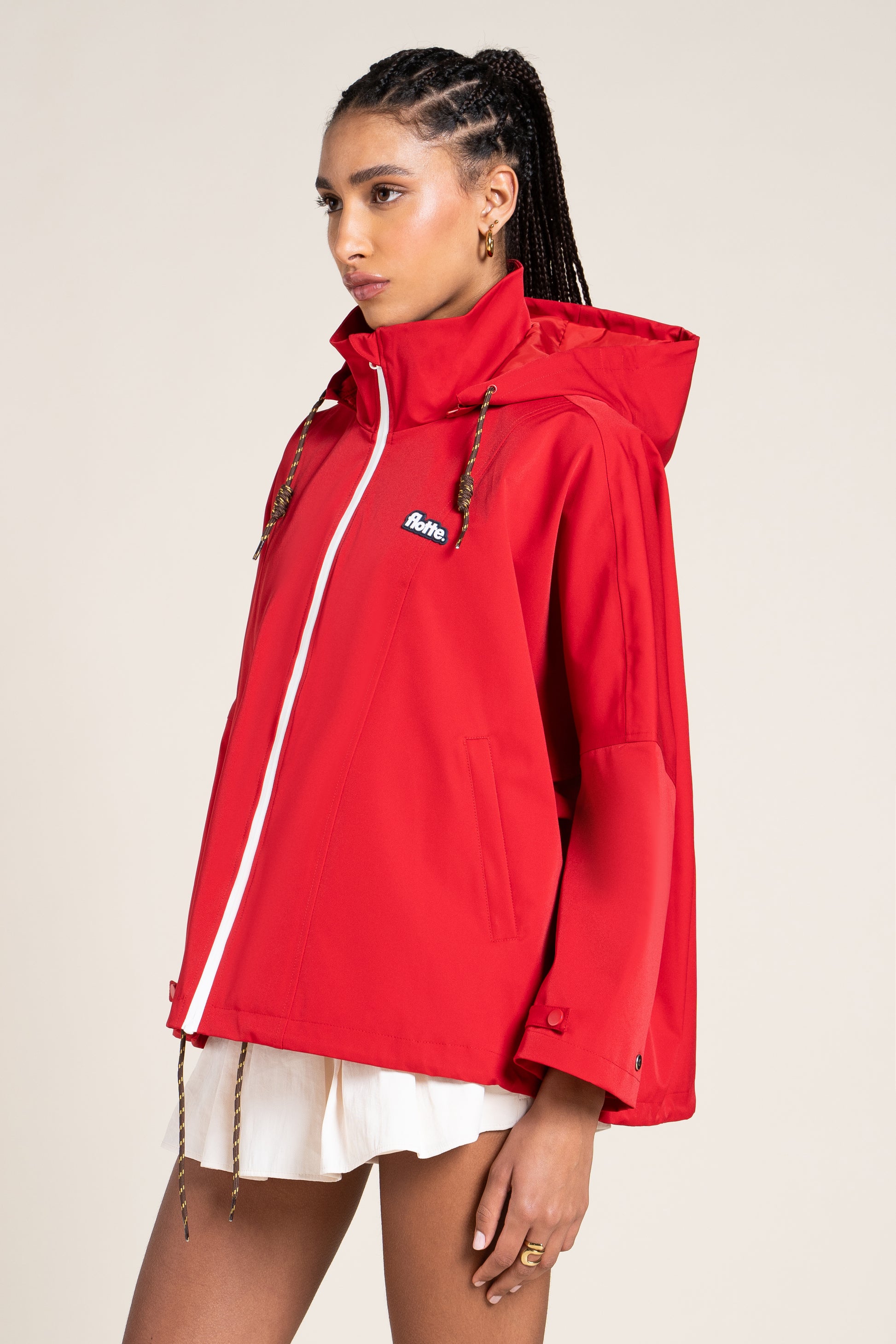 A woman wearing a bright red Flotte waterproof hooded jacket with a white zipper.
