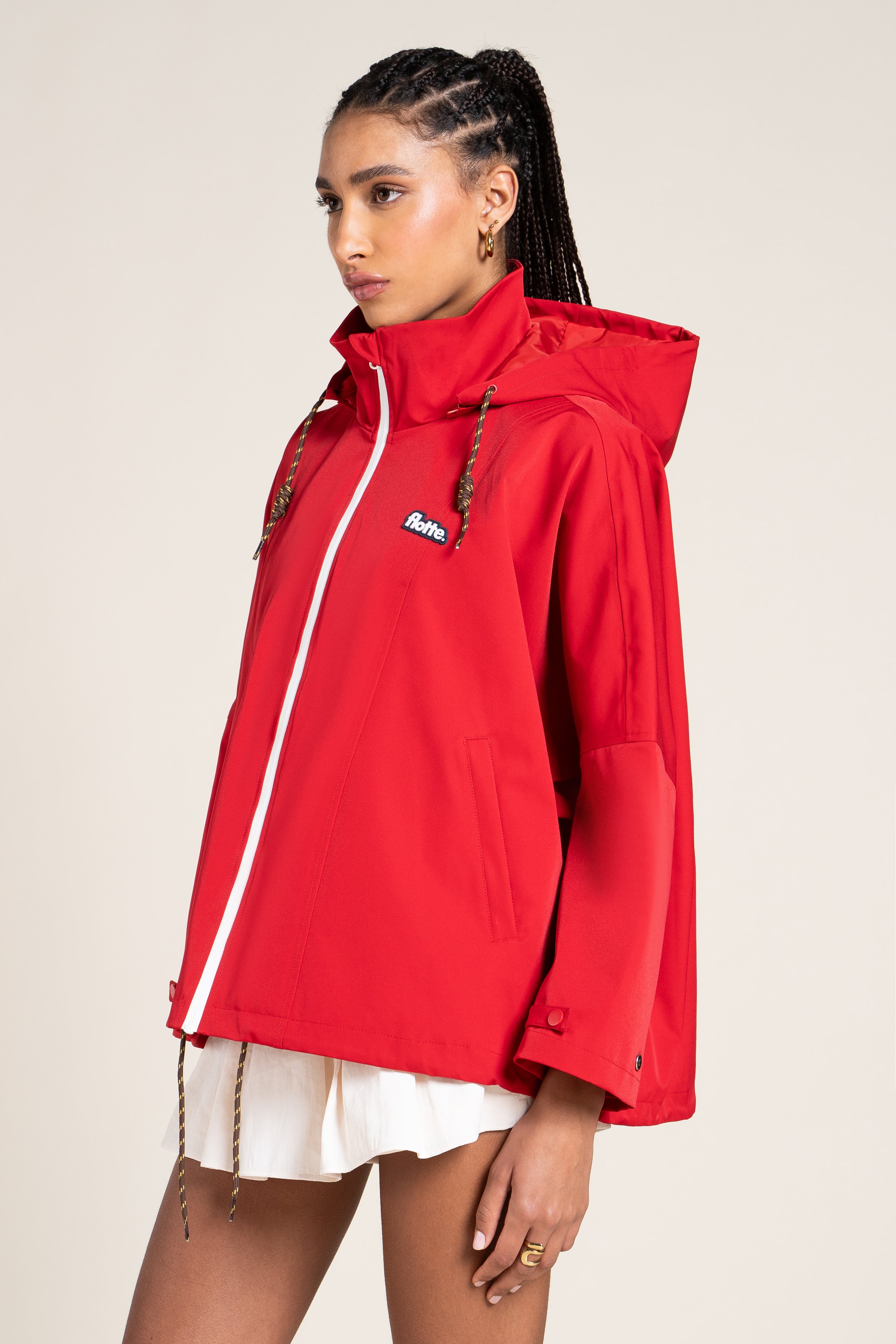 A woman wearing a bright red Flotte waterproof hooded jacket with a white zipper.