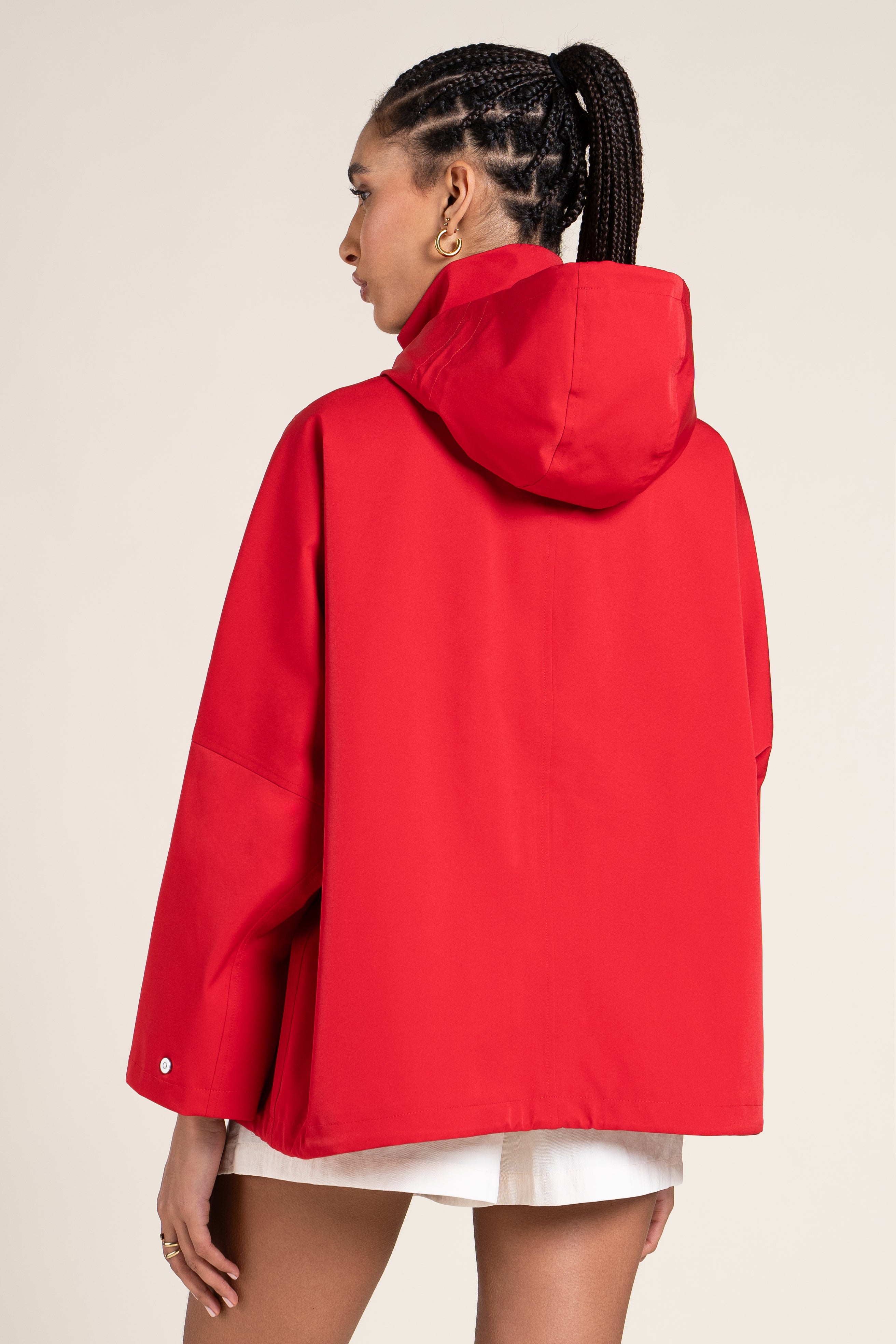 Woman wearing a bright red hooded jacket against a neutral background.