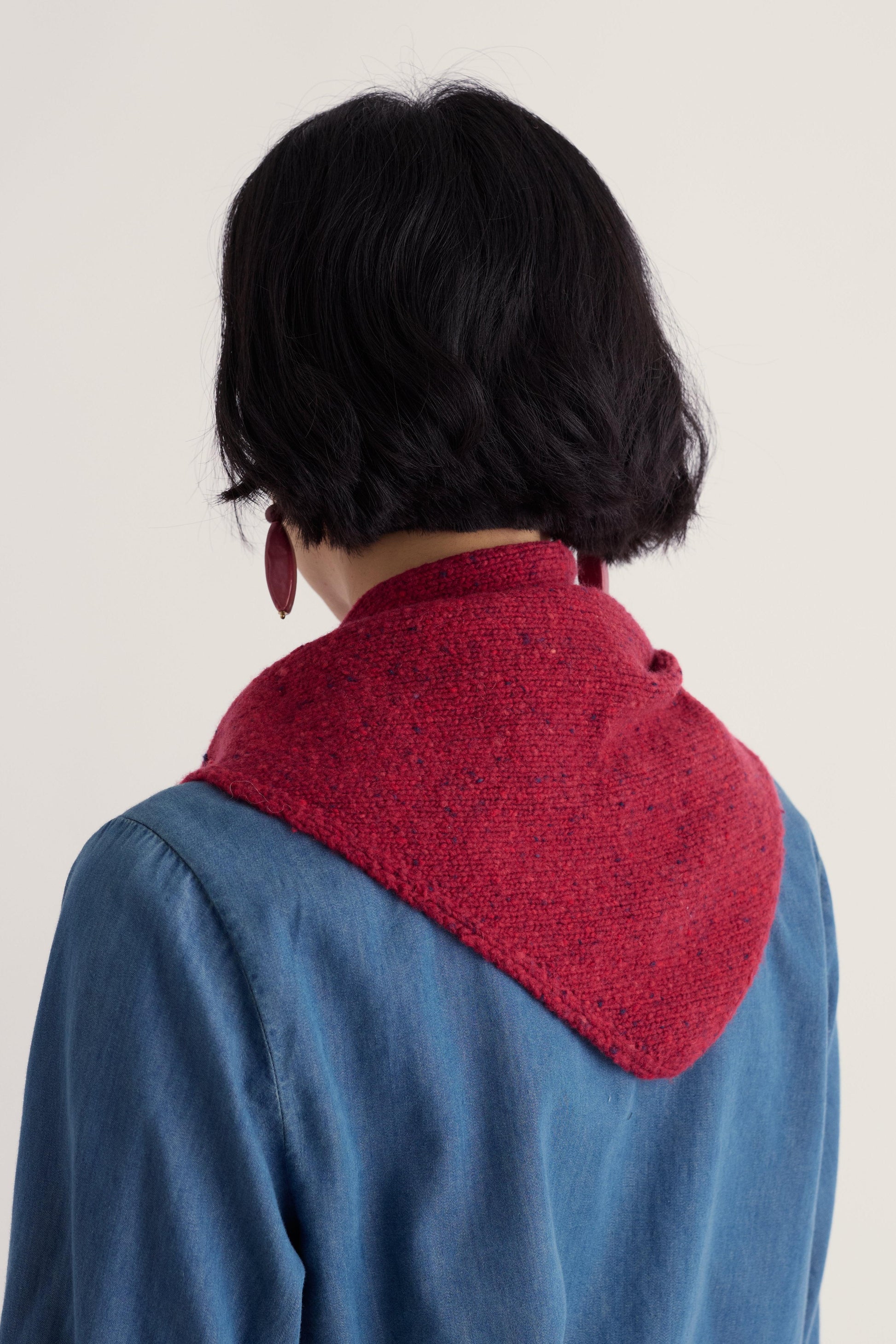 A person with short dark hair wearing a textured red Seasalt wool knit scarf over a blue shirt.