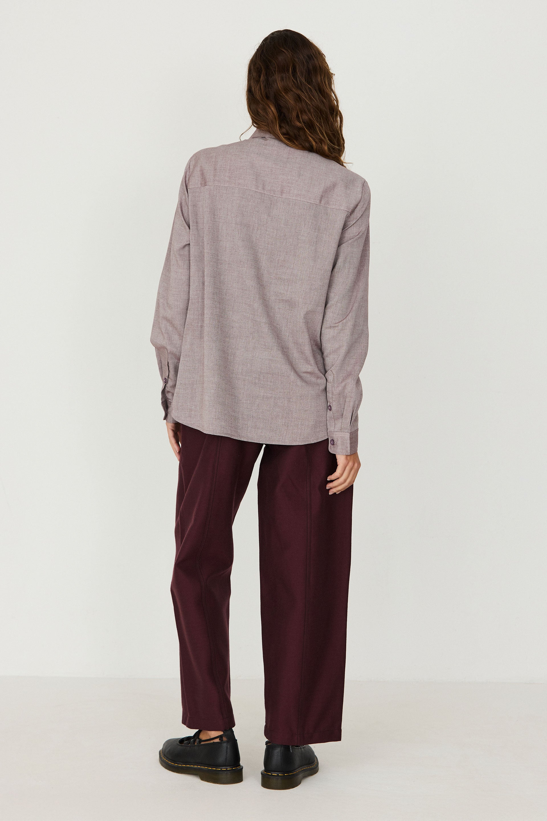 Woman seen from behind wearing a red melange casual shirt and dark trousers against a plain background.