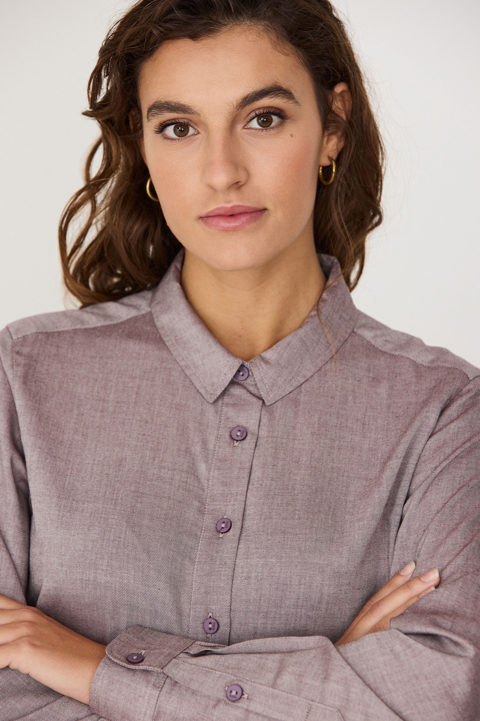 Woman with wavy hair wearing a red melange SKFK button-up shirt with arms crossed.