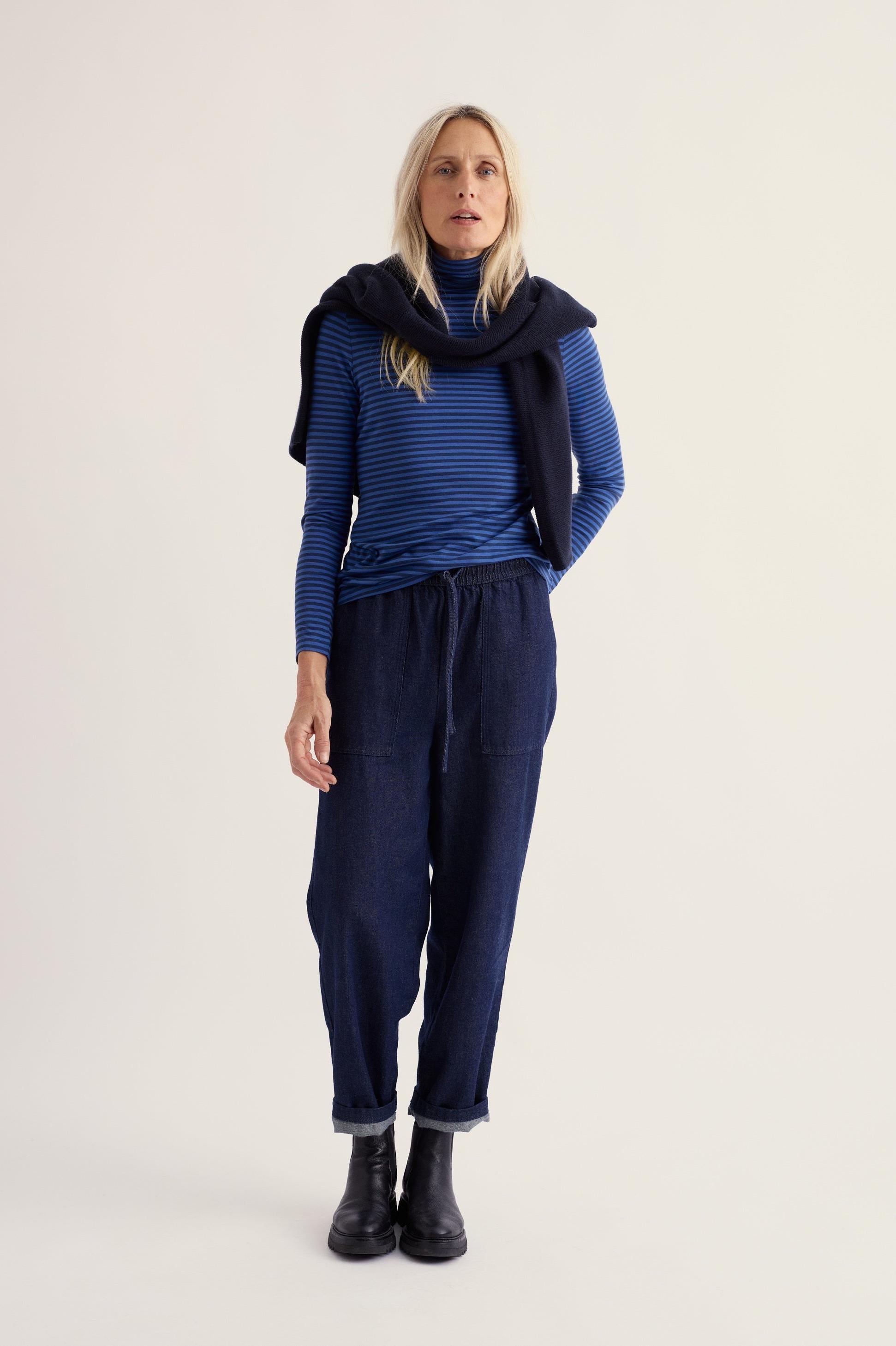 A woman wearing a blue stripe rollneck organic cotton top and dark trousers against a plain background.
