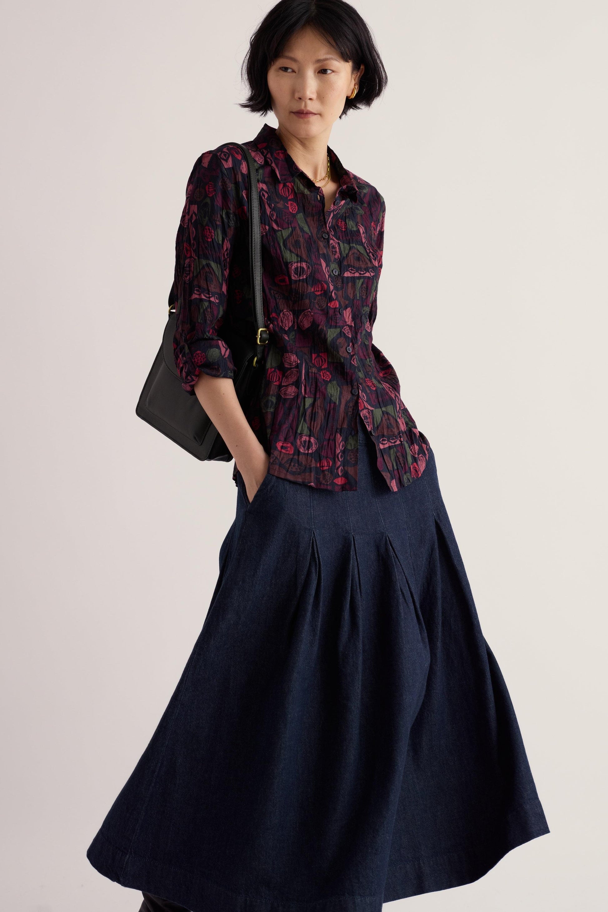 A woman wearing a dark floral Seasalt Cornwall Larissa organic cotton shirt with a long denim skirt.