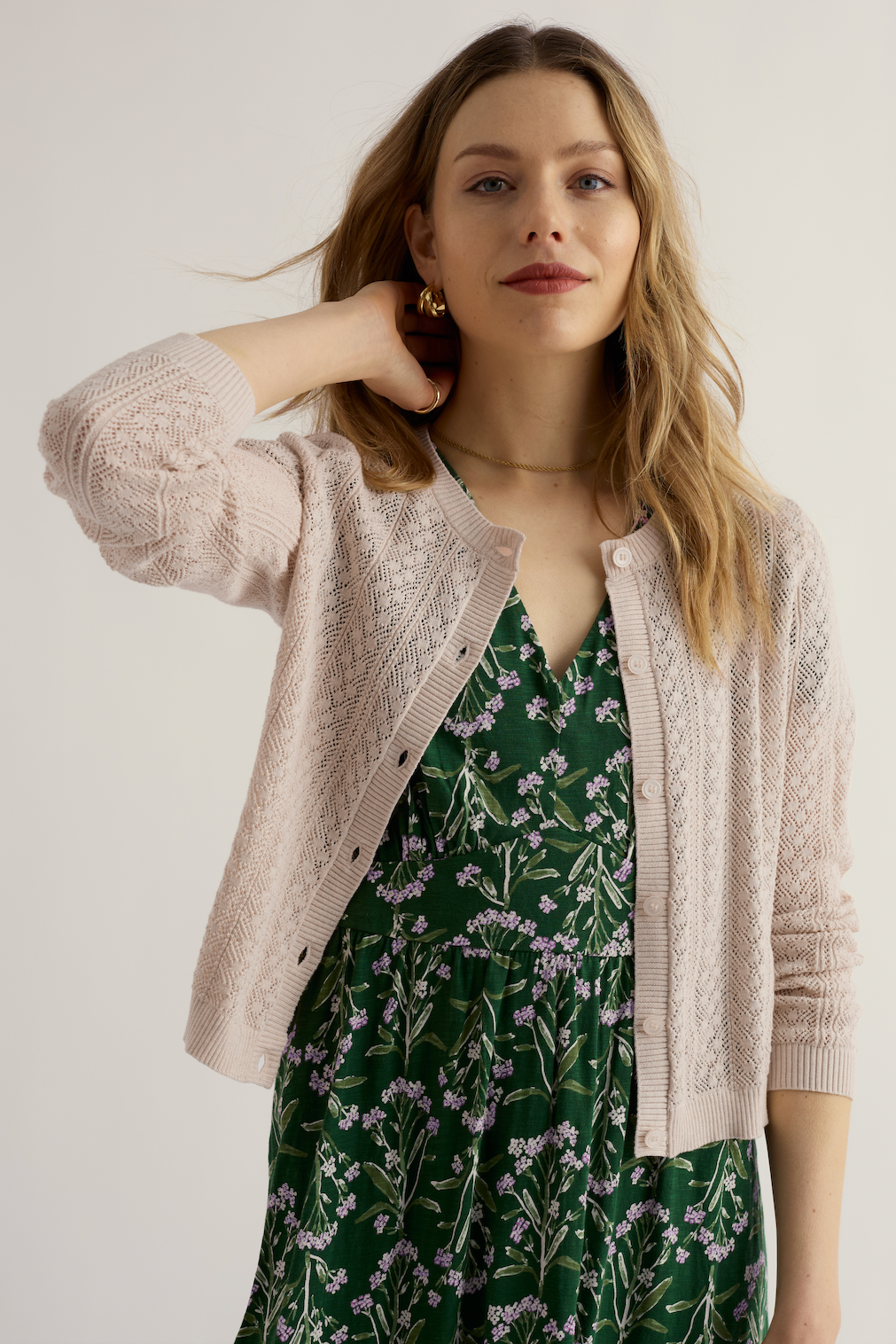 A woman wearing a Seasalt organic cotton cardigan over a green floral dress against a neutral background.