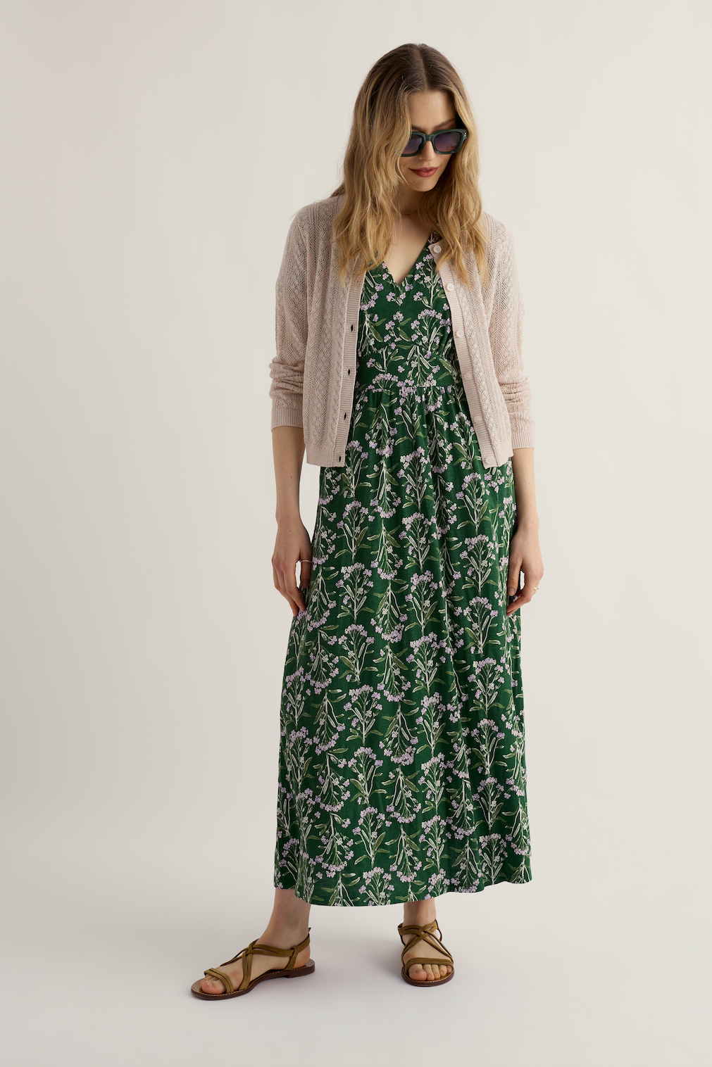 A woman wearing a green Seasalt organic cotton floral print maxi dress with a beige cardigan and sunglasses.