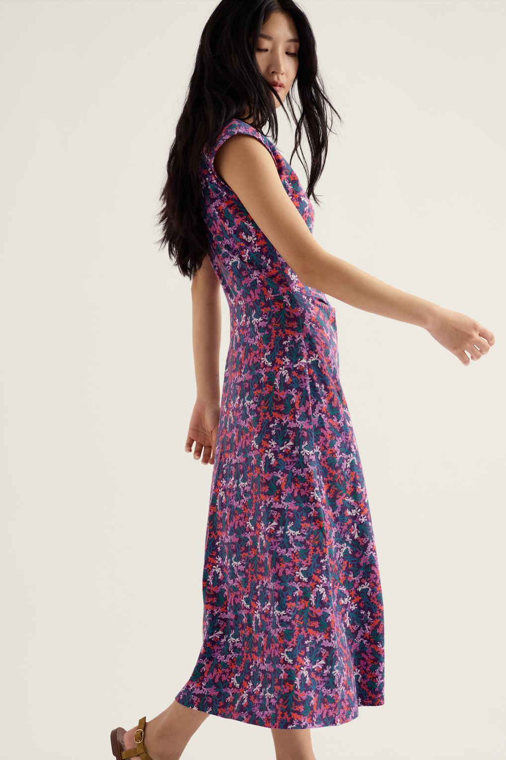 A woman wearing a Seasalt organic cotton floral midi dress against a neutral background.