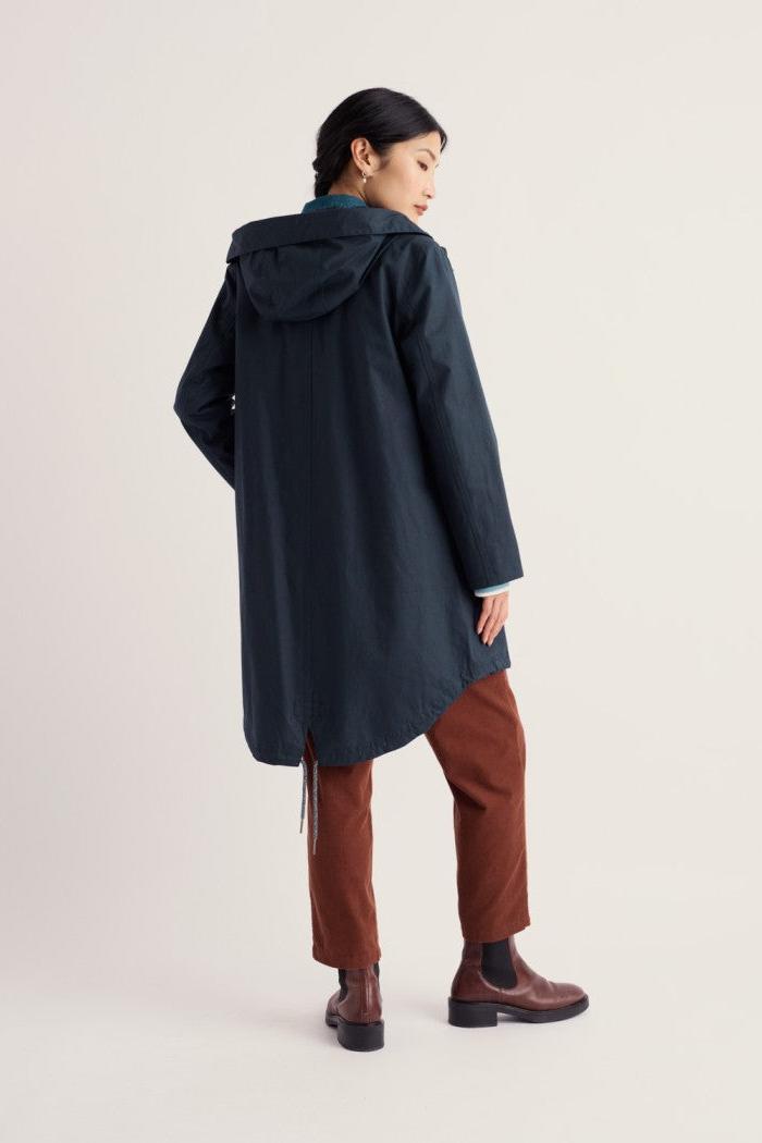 A model shown from the back wearing a dark navy hooded coat, brown trousers, and brown Chelsea boots against a plain light beige studio background.
