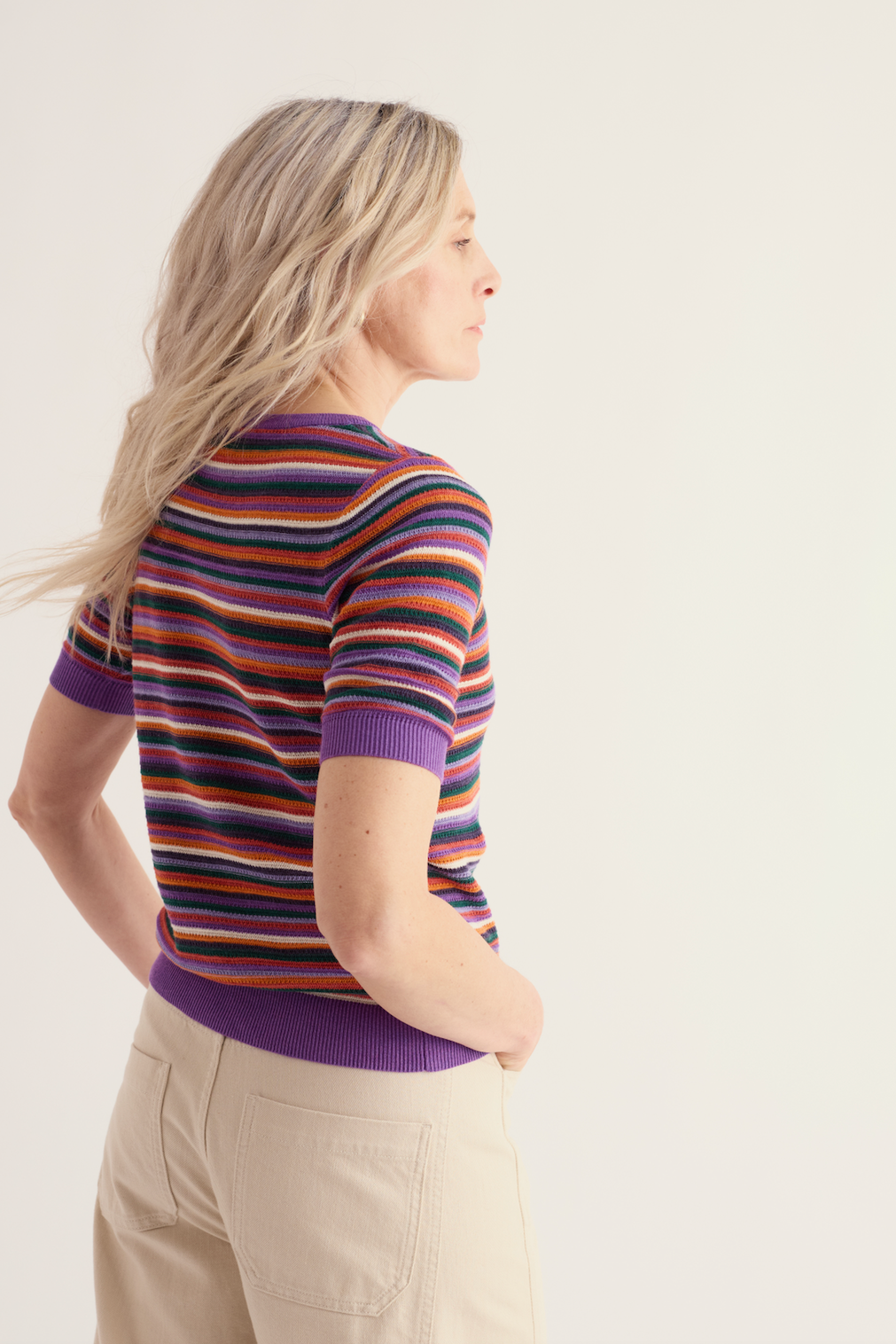 Woman wearing a colorful striped Seasalt organic cotton short-sleeve top against a neutral background.