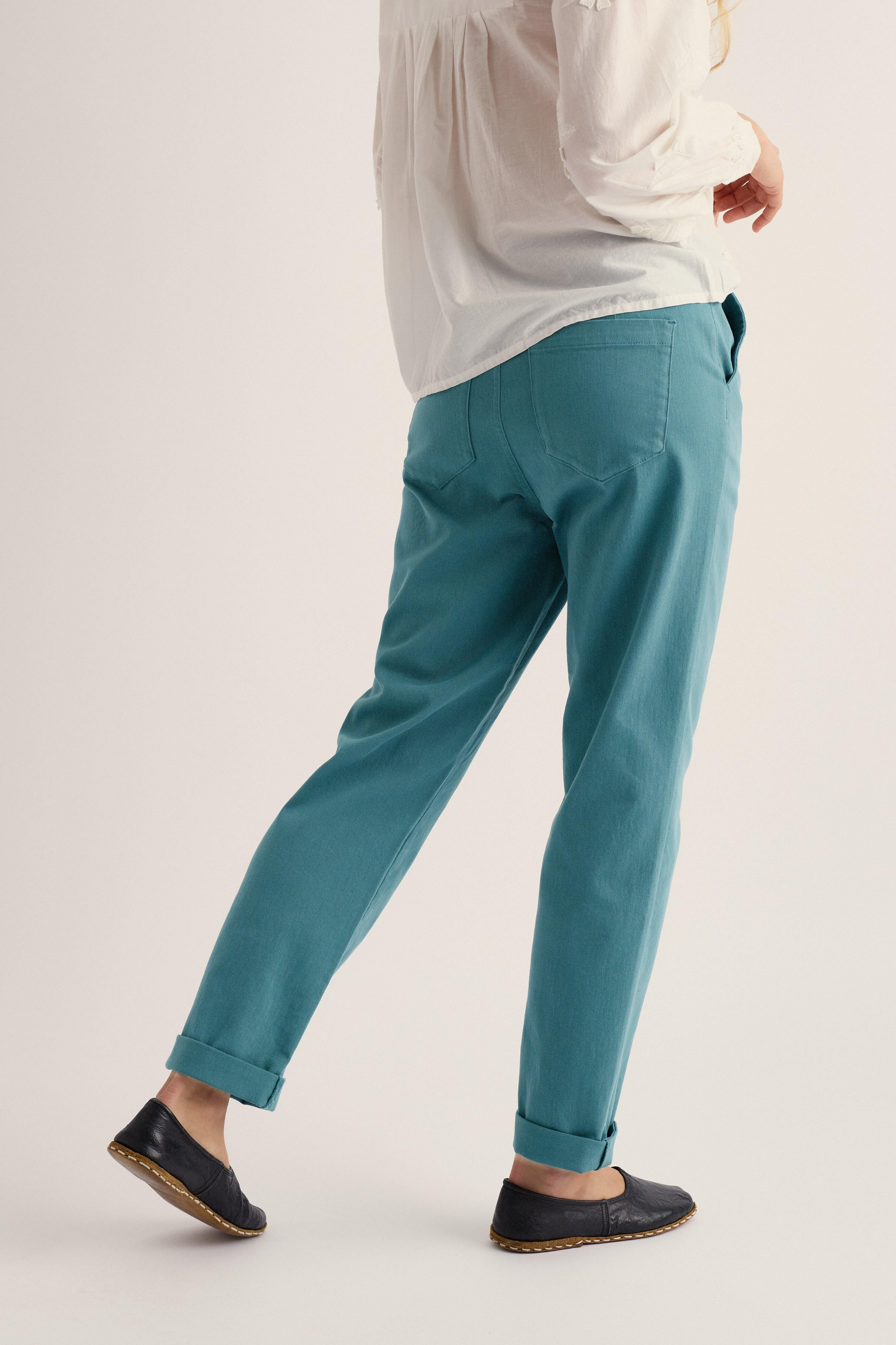 Person wearing organic cotton teal pants and a white shirt on a plain background