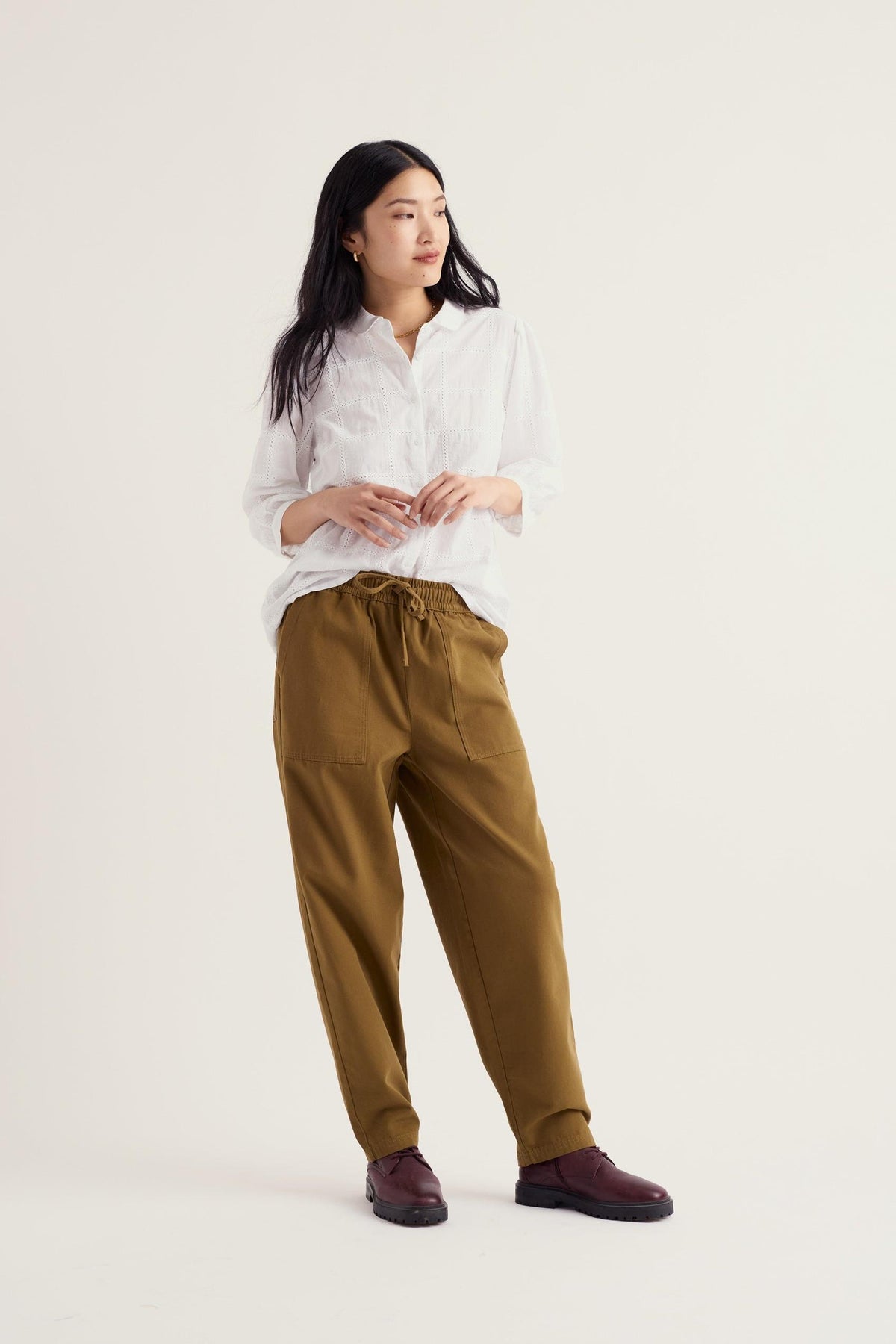 A model wearing a white embroidered organic cotton blouse by Seasalt Cornwall with olive trousers.