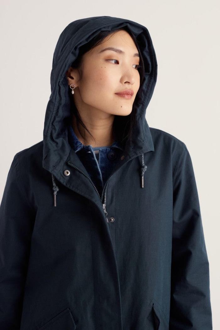A woman wearing a dark navy hooded jacket with a snap-button front and drawstrings, photographed against a plain light background.