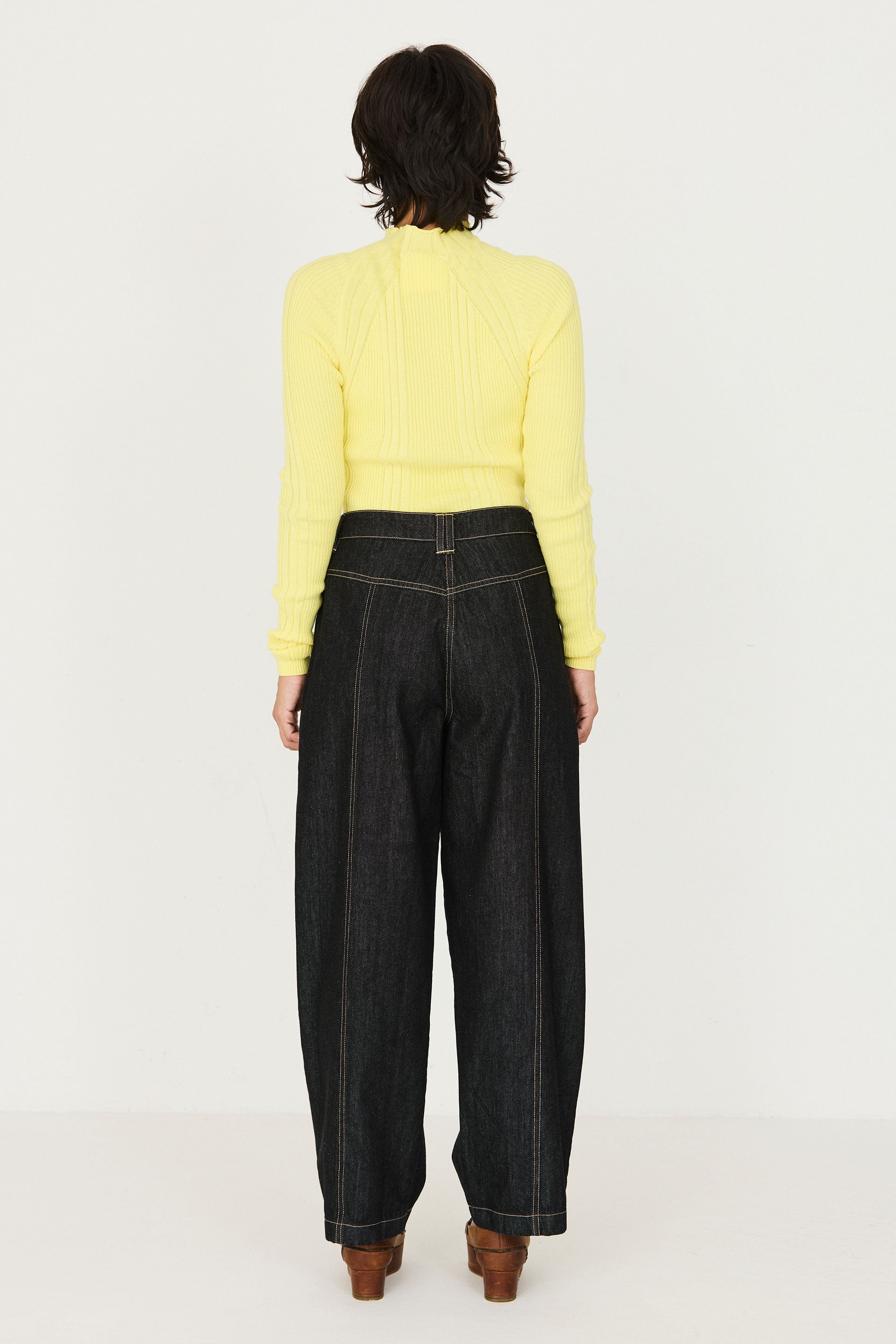 Woman standing from behind wearing a yellow ribbed top and SKFK barrel leg black denim jeans against a plain background.