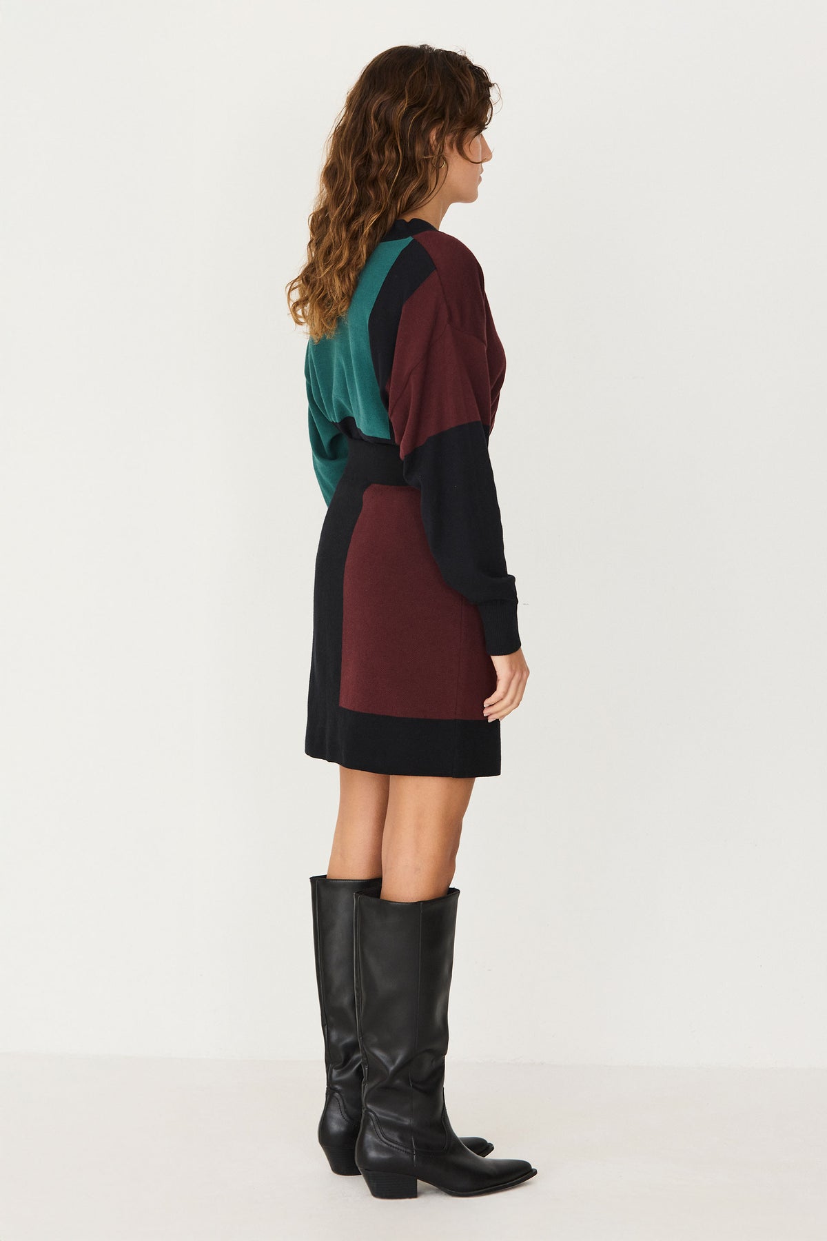 Woman standing in a profile pose wearing a SKFK colourblock winter skirt coord outfit and black knee-high boots.