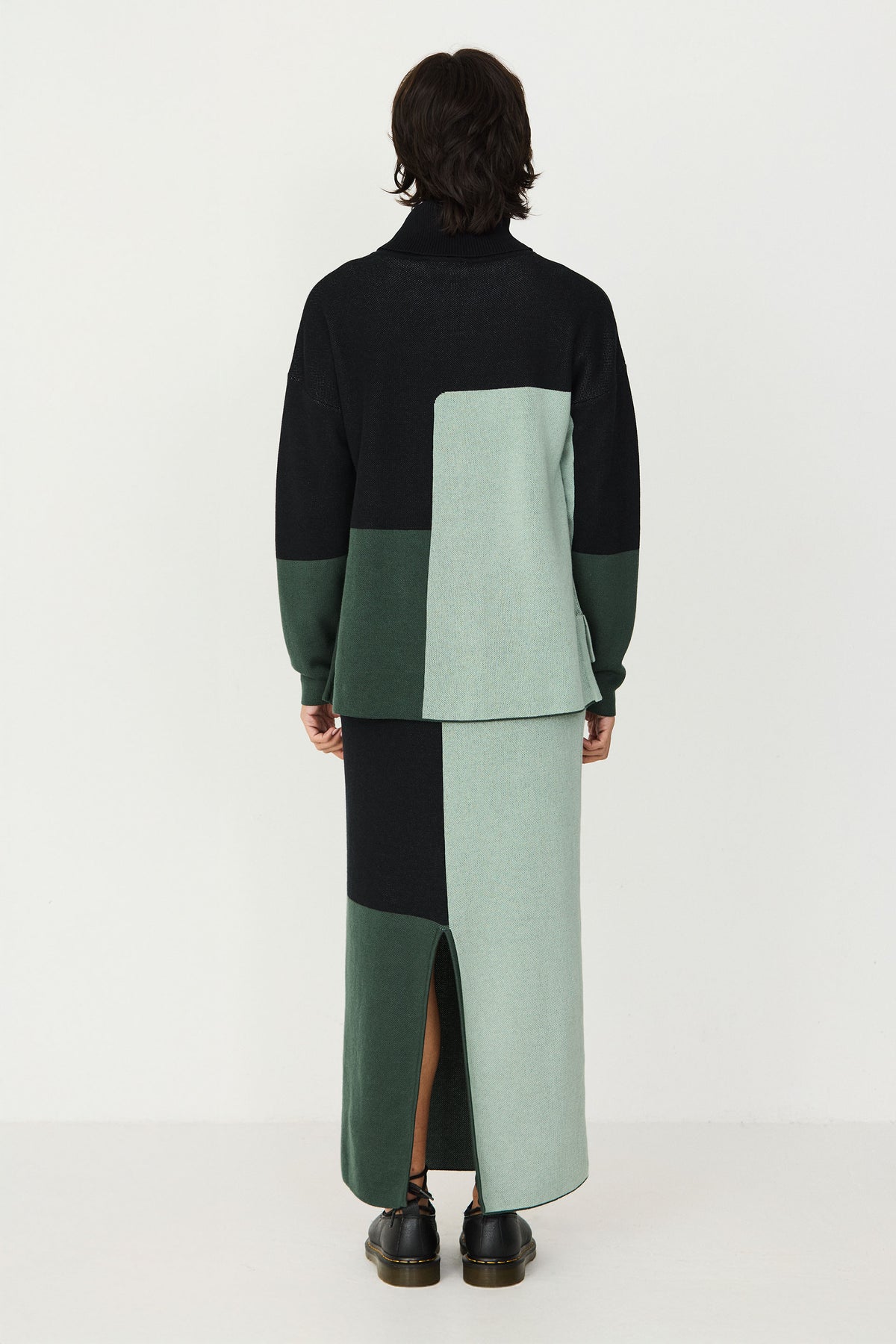 Model wearing a colour-blocked black and green cotton knit turtleneck sweater and matching long skirt.