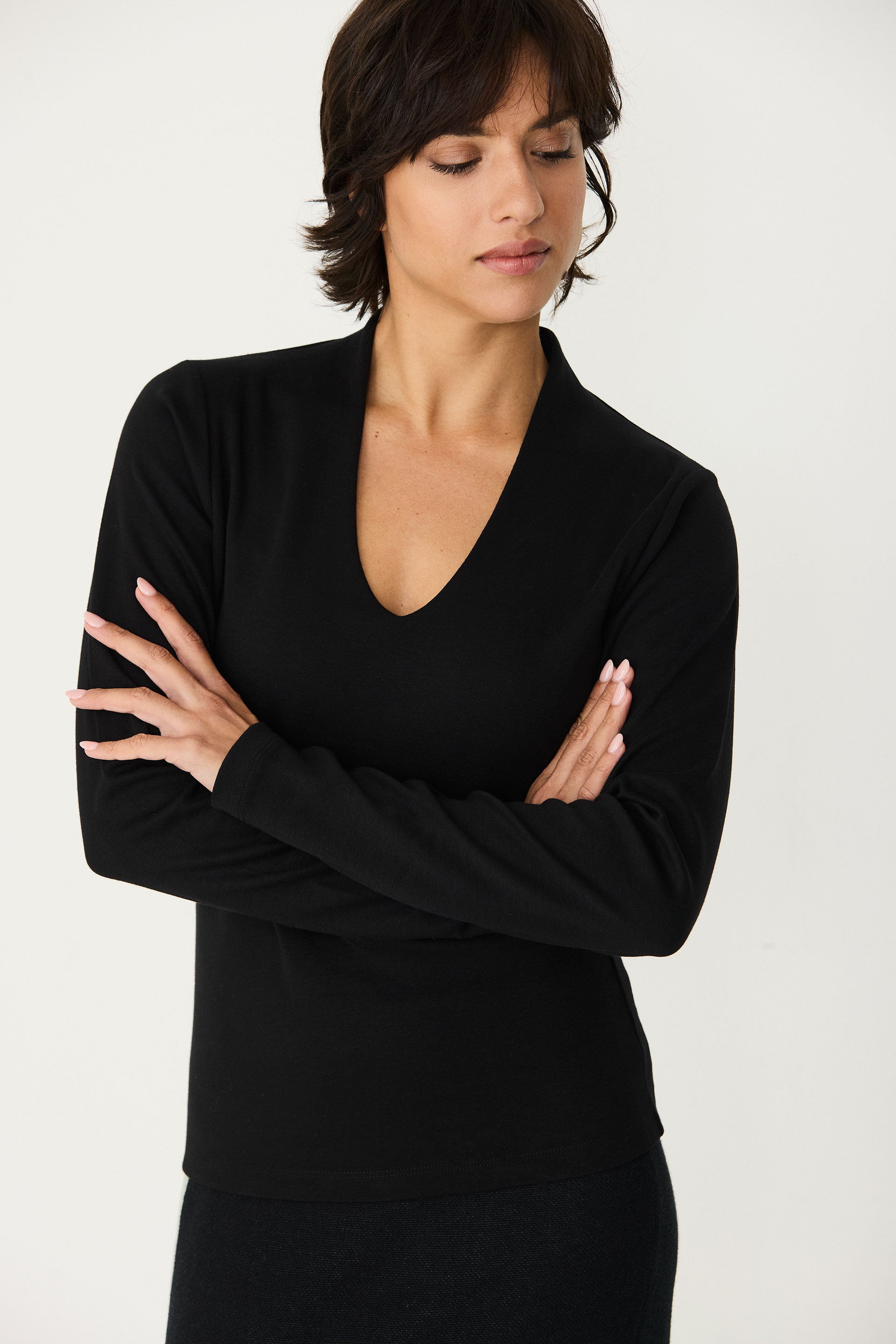 A woman with short hair posing in a SKFK organic cotton black long sleeve top with a V-neckline.