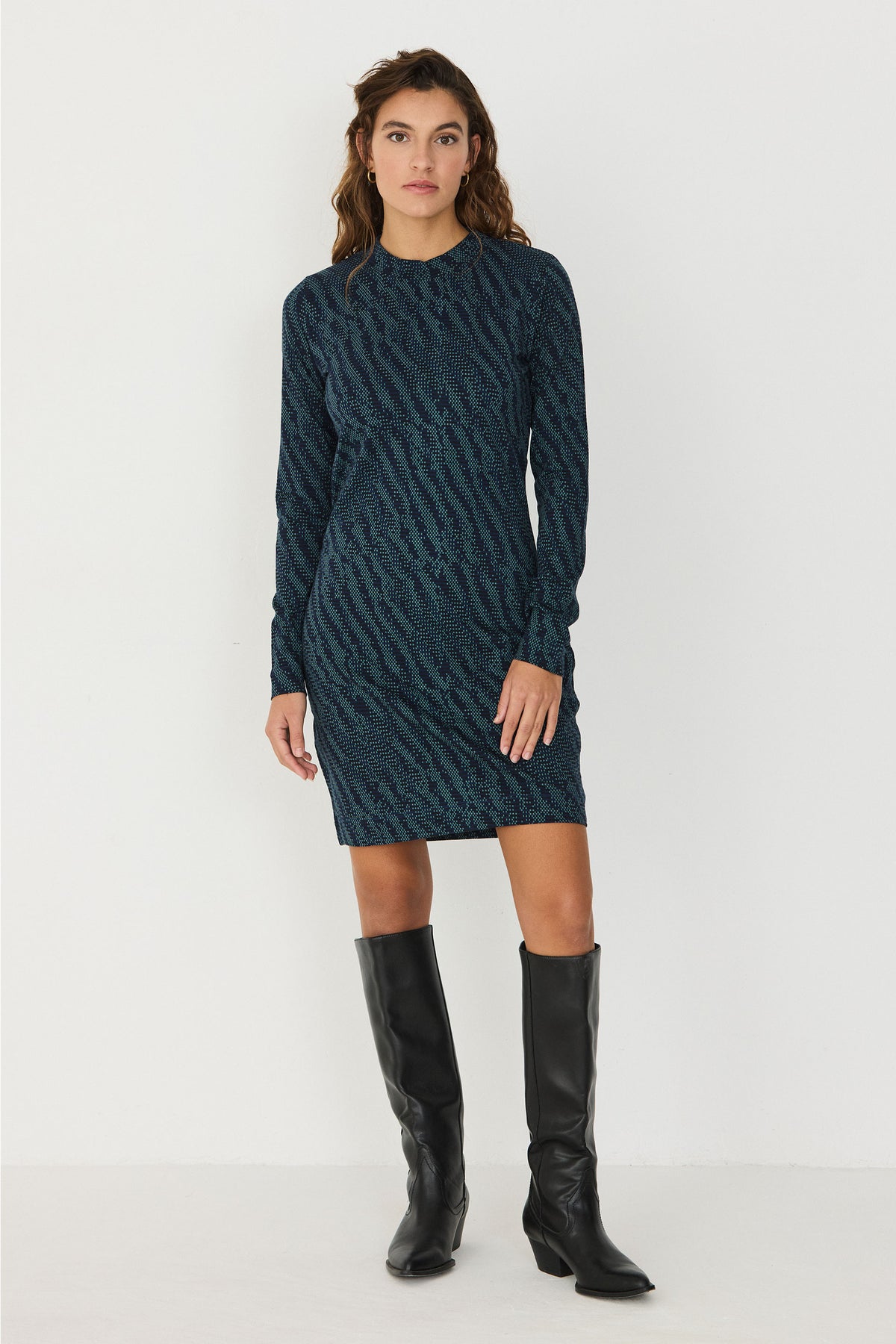 Woman posing in a patterned SKFK long-sleeved green casual dress paired with black knee-high boots.