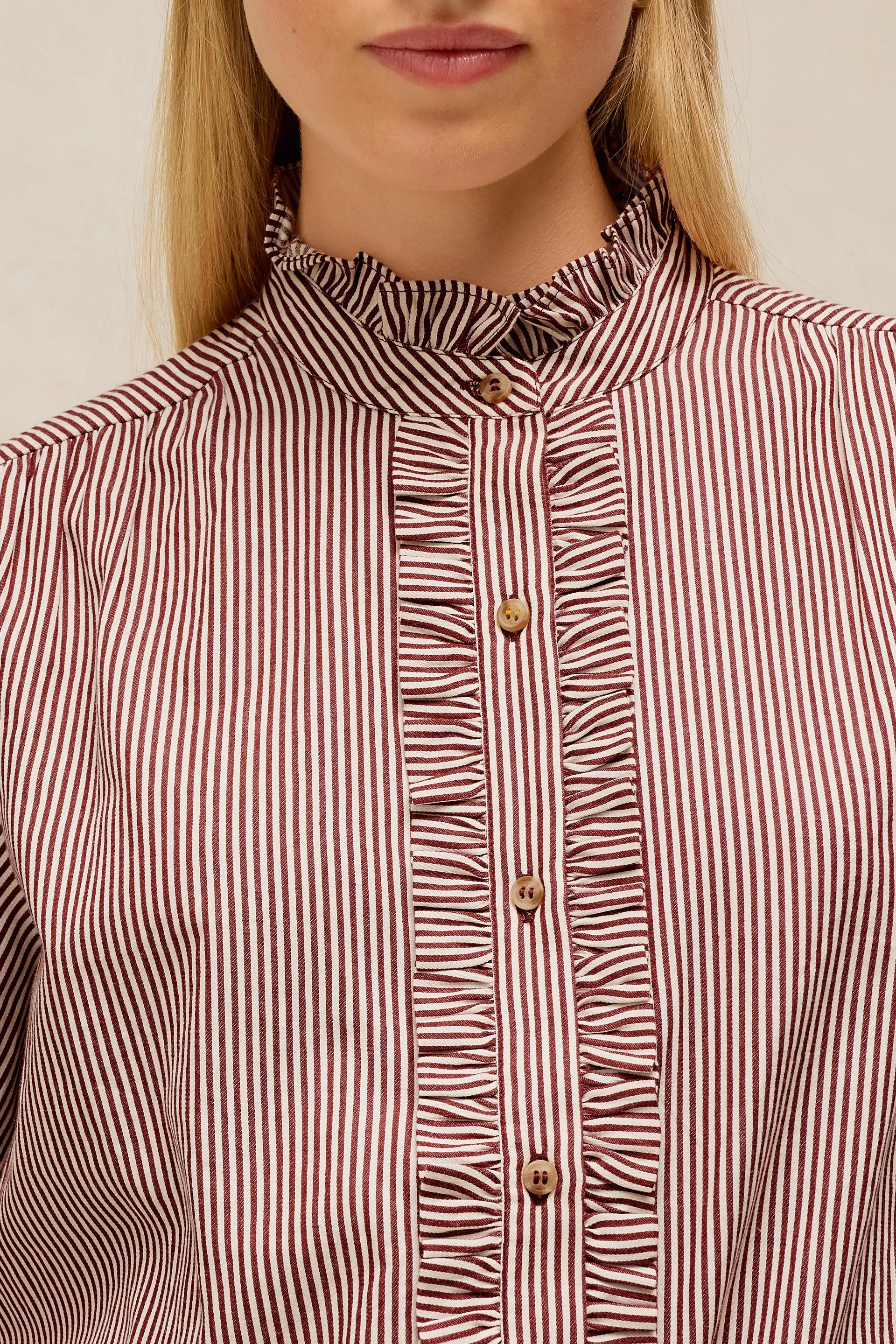 Close-up of a woman wearing a ruffled high-neck blouse with vertical red and white stripes and gold buttons.