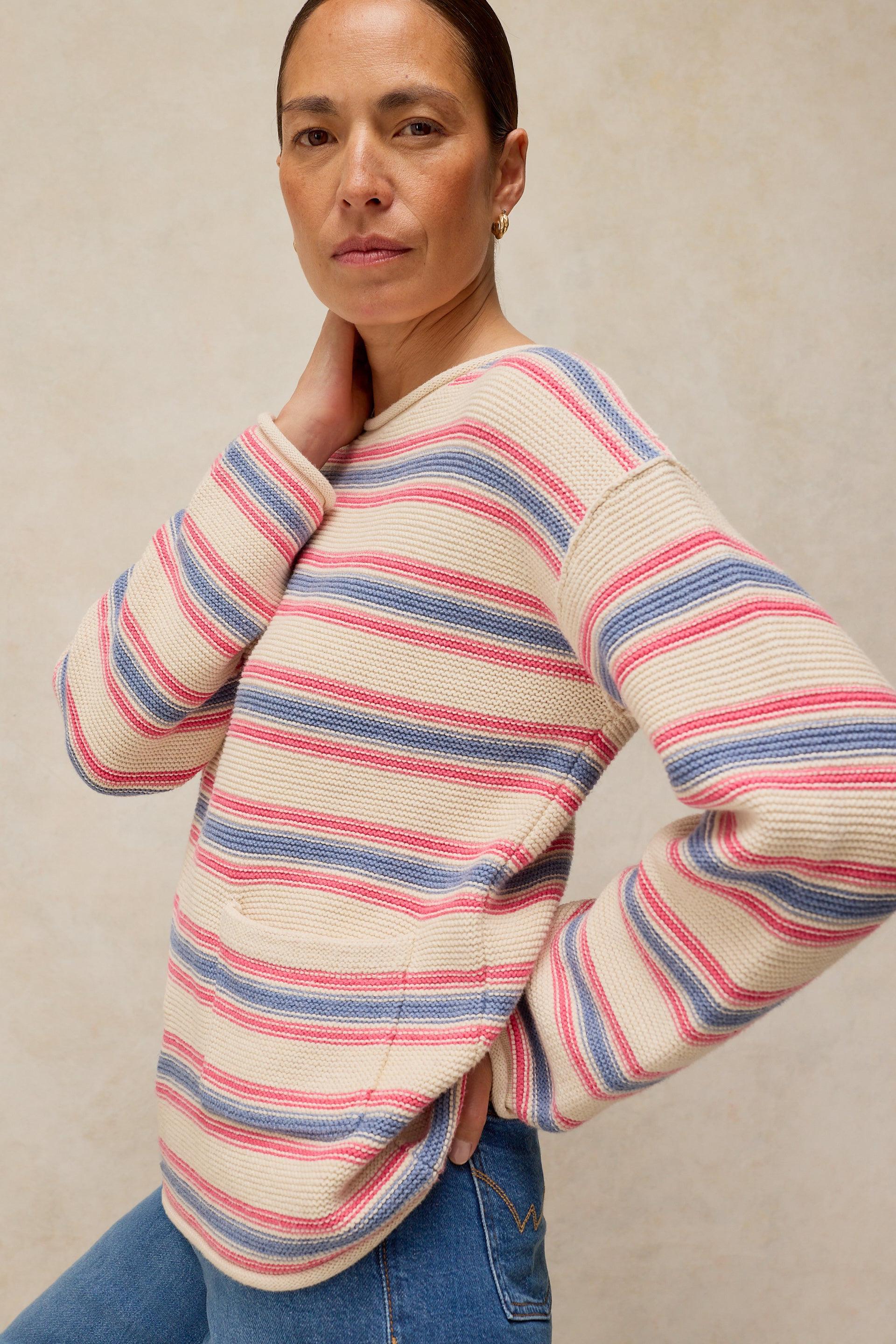 A woman posing in a cream-colored sweater with pink and blue stripes made of organic cotton.