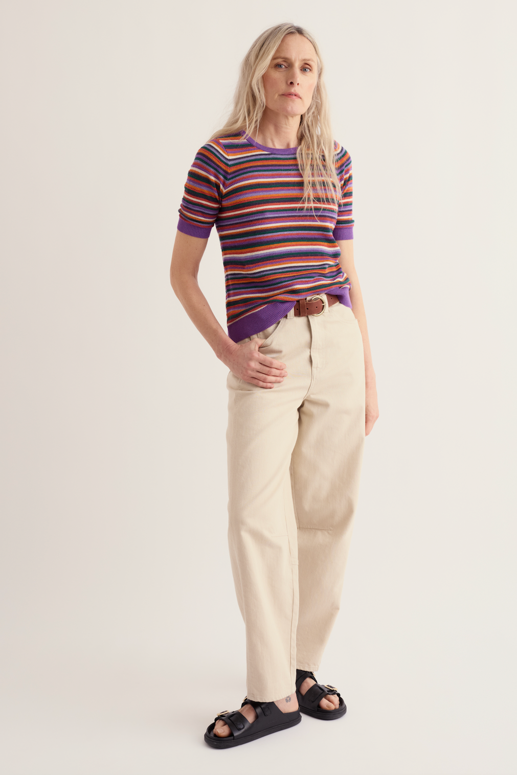 Woman wearing a multi-colored striped organic cotton top and beige trousers.