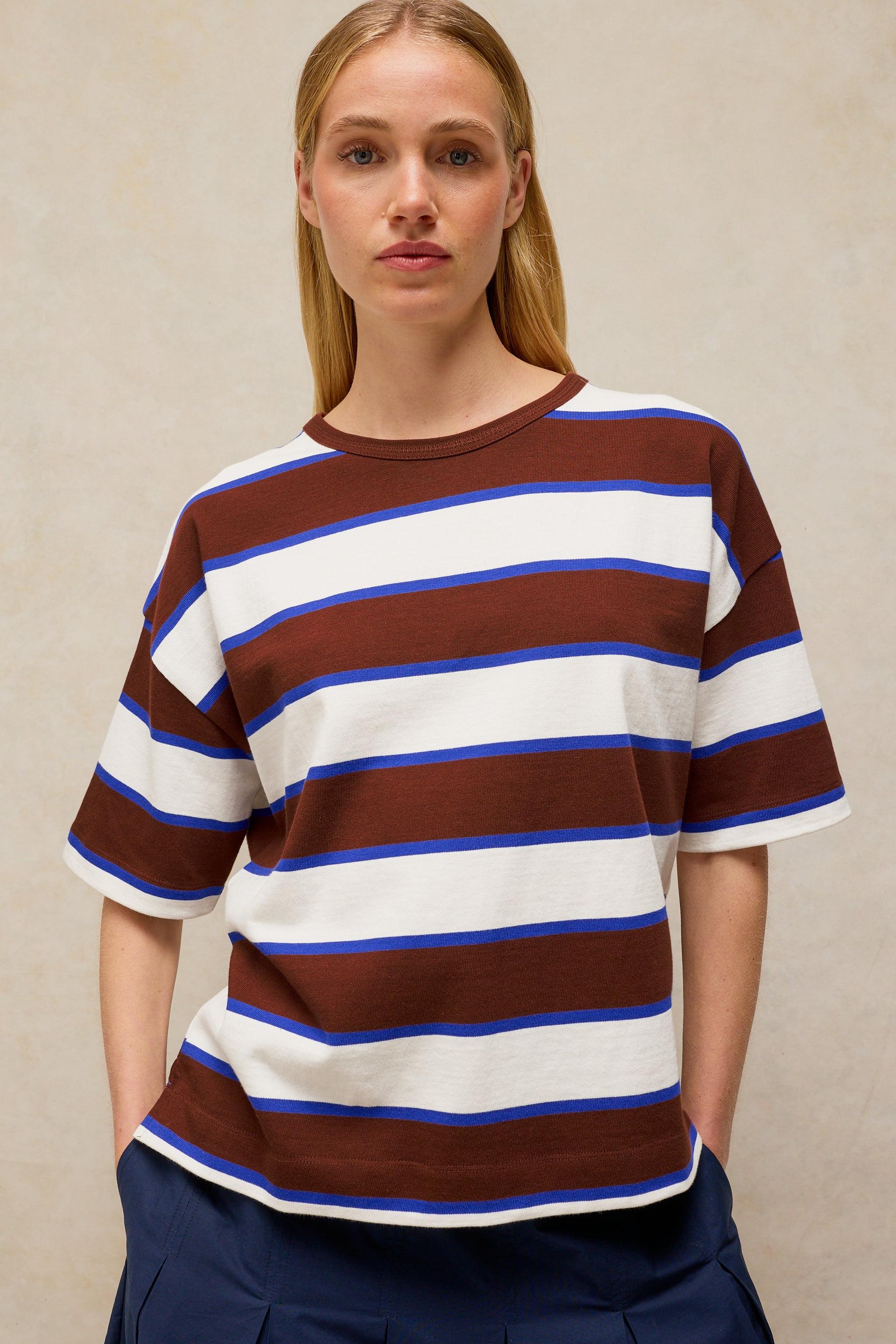 A woman wearing a brown, blue, and white striped organic cotton t-shirt against a neutral background.