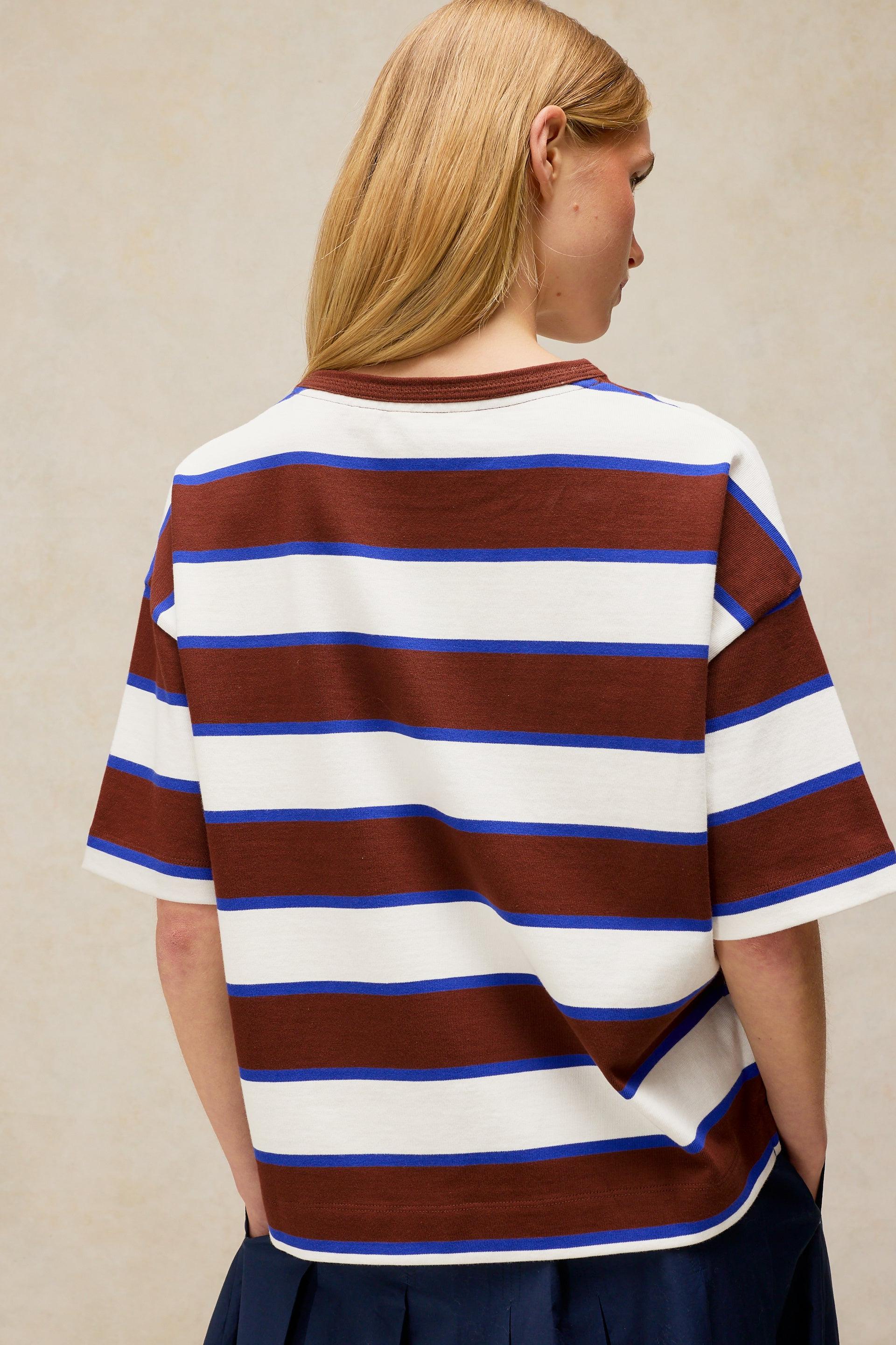 Woman seen from behind wearing a white, brown, and blue striped organic cotton t-shirt against a neutral background.