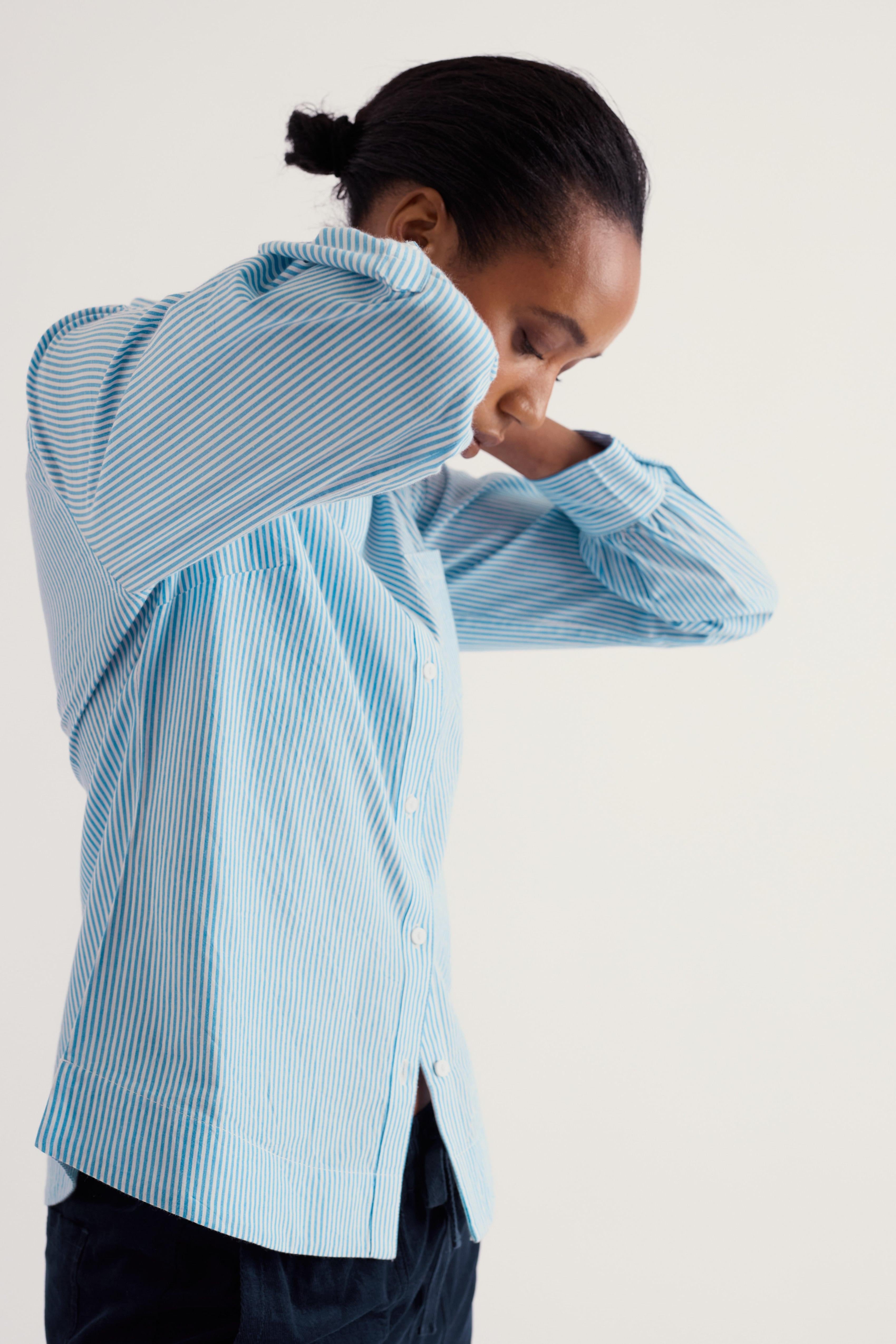 A person wearing a light blue and white vertically striped button-up shirt, shown from the waist up against a plain light background.