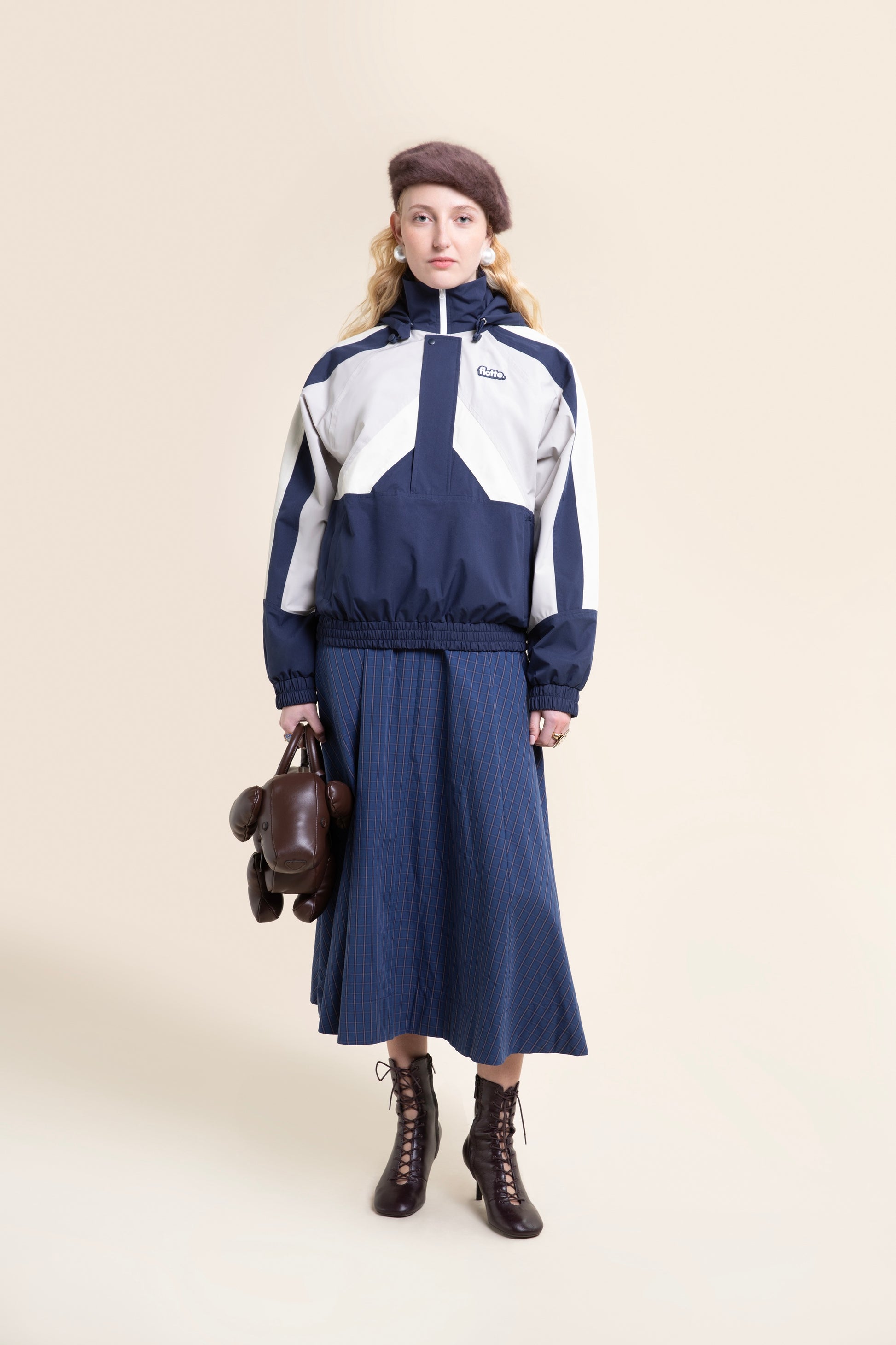Woman posing in a navy and white color-blocked waterproof recycled polyester coat against a plain beige background.