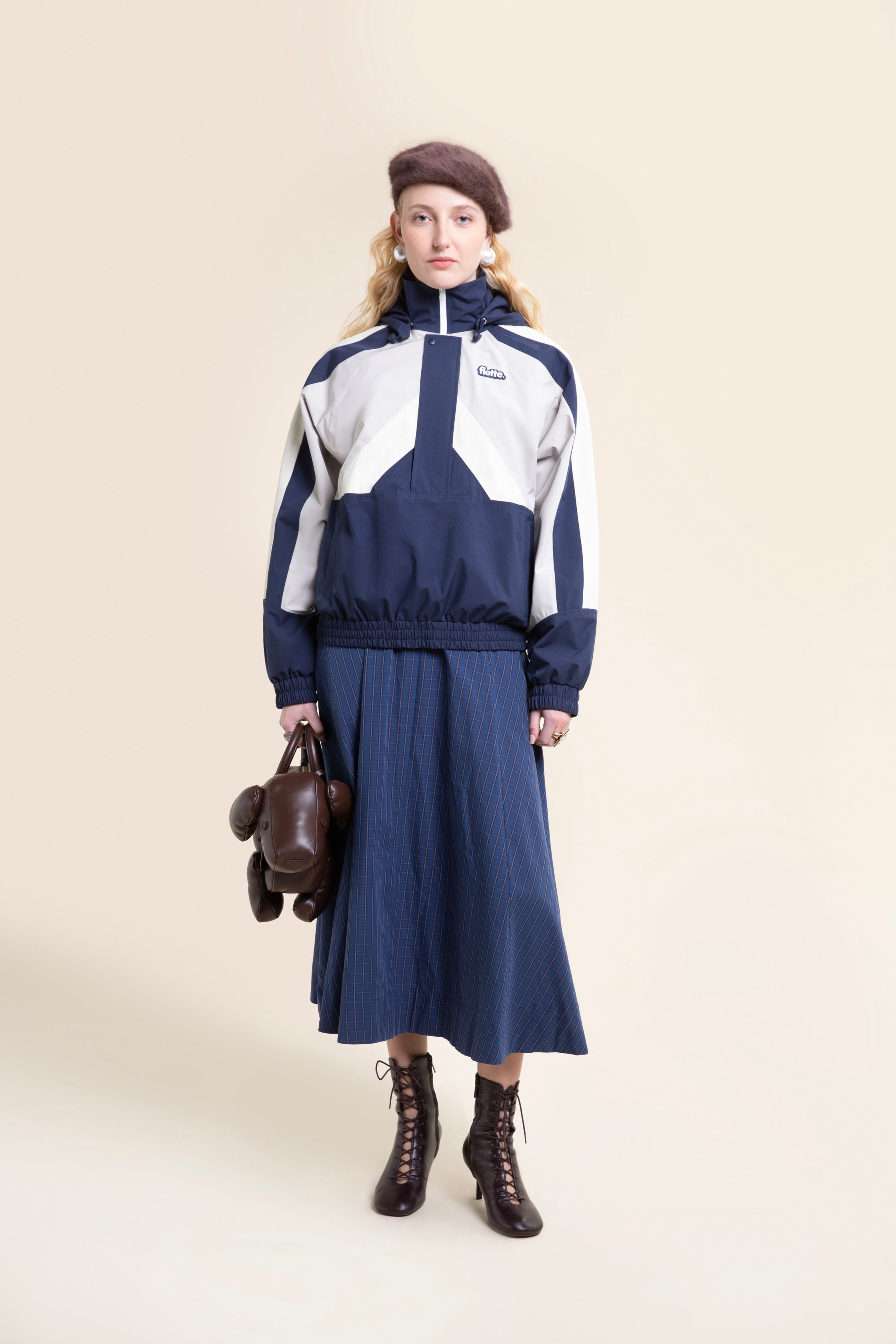 Woman posing in a navy and white color-blocked waterproof recycled polyester coat against a plain beige background.