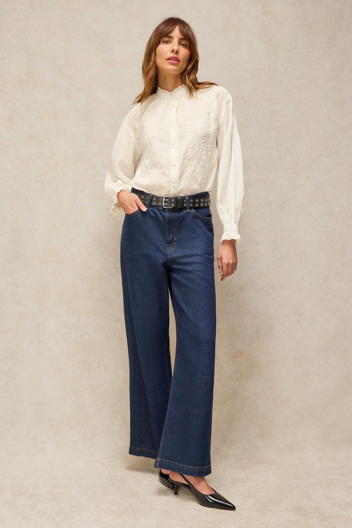 Woman posing in a white embroidered organic cotton blouse and wide-leg dark blue jeans.
