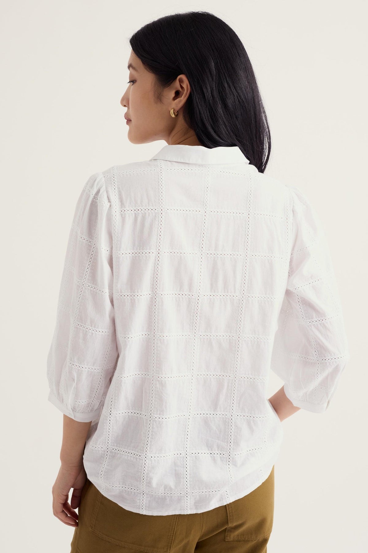 Woman seen from behind wearing a white organic cotton blouse with intricate embroidery detail.
