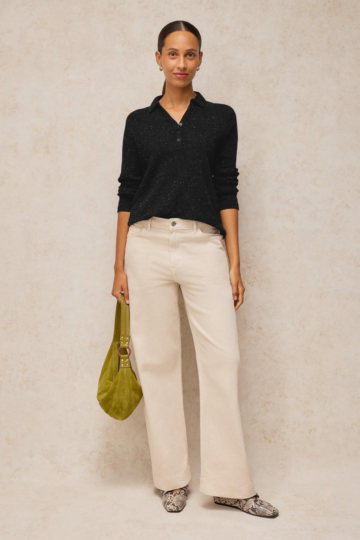 Woman standing wearing a black White Stuff sparkle polo top and cream wide-leg trousers.