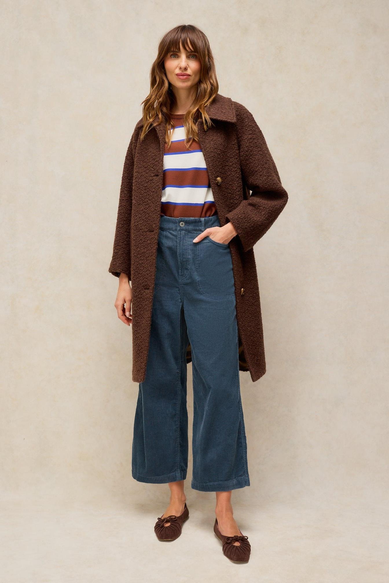 Woman wearing White Stuff blue cord trousers with a textured brown coat and striped top.