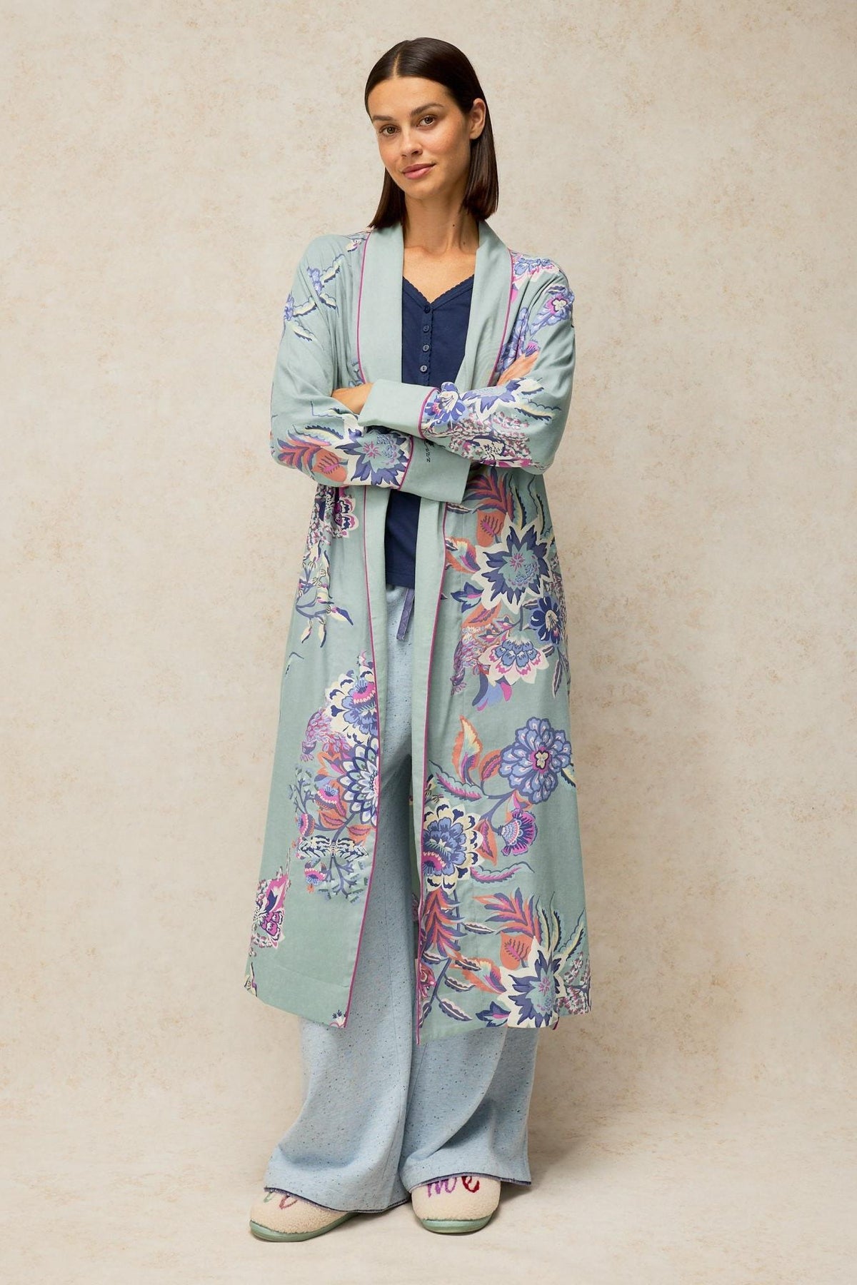 A woman standing with arms crossed wearing a long blue floral pattern White Stuff dressing gown over pyjamas.