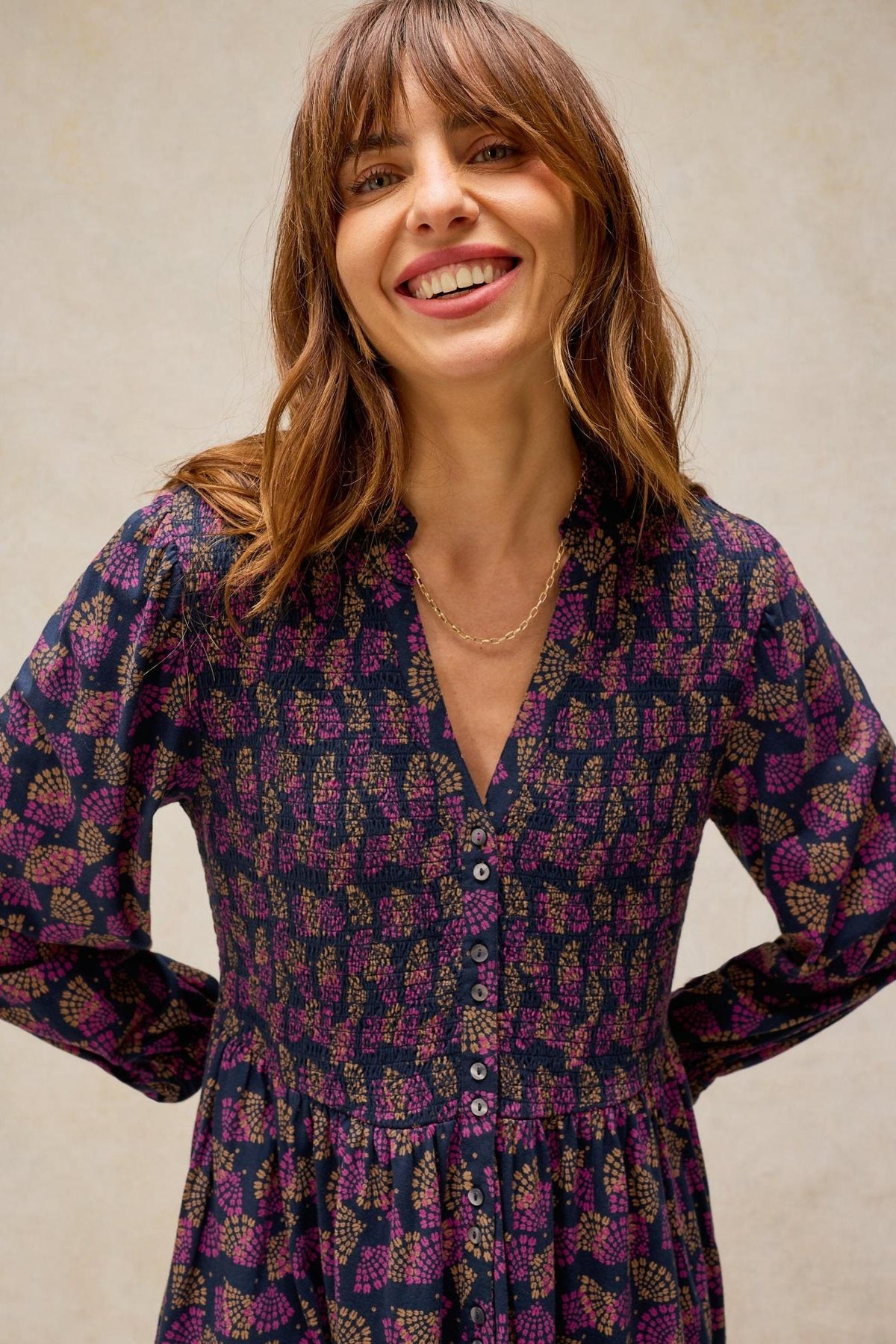 A woman smiling in a dark-patterned White Stuff everyday dress with button-down detail.