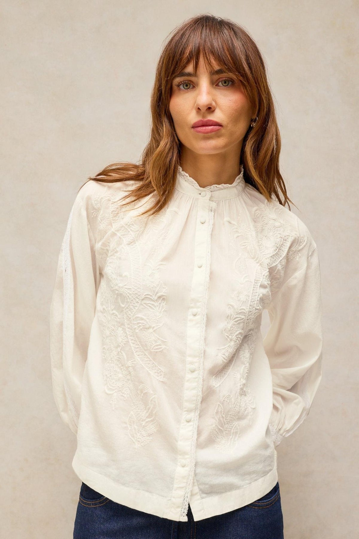 A woman posing in a long-sleeved white embroidered organic cotton blouse from White Stuff.