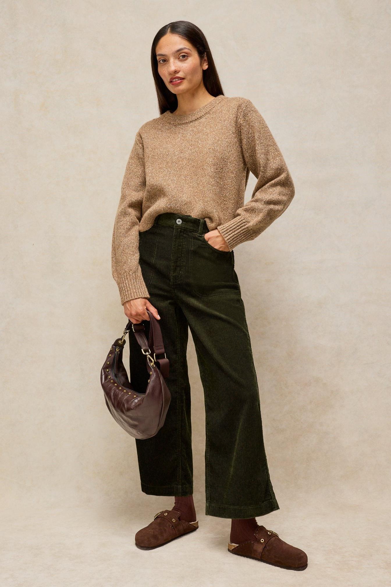 Woman posing in a tan sweater and green White Stuff cord trousers with a dark leather bag