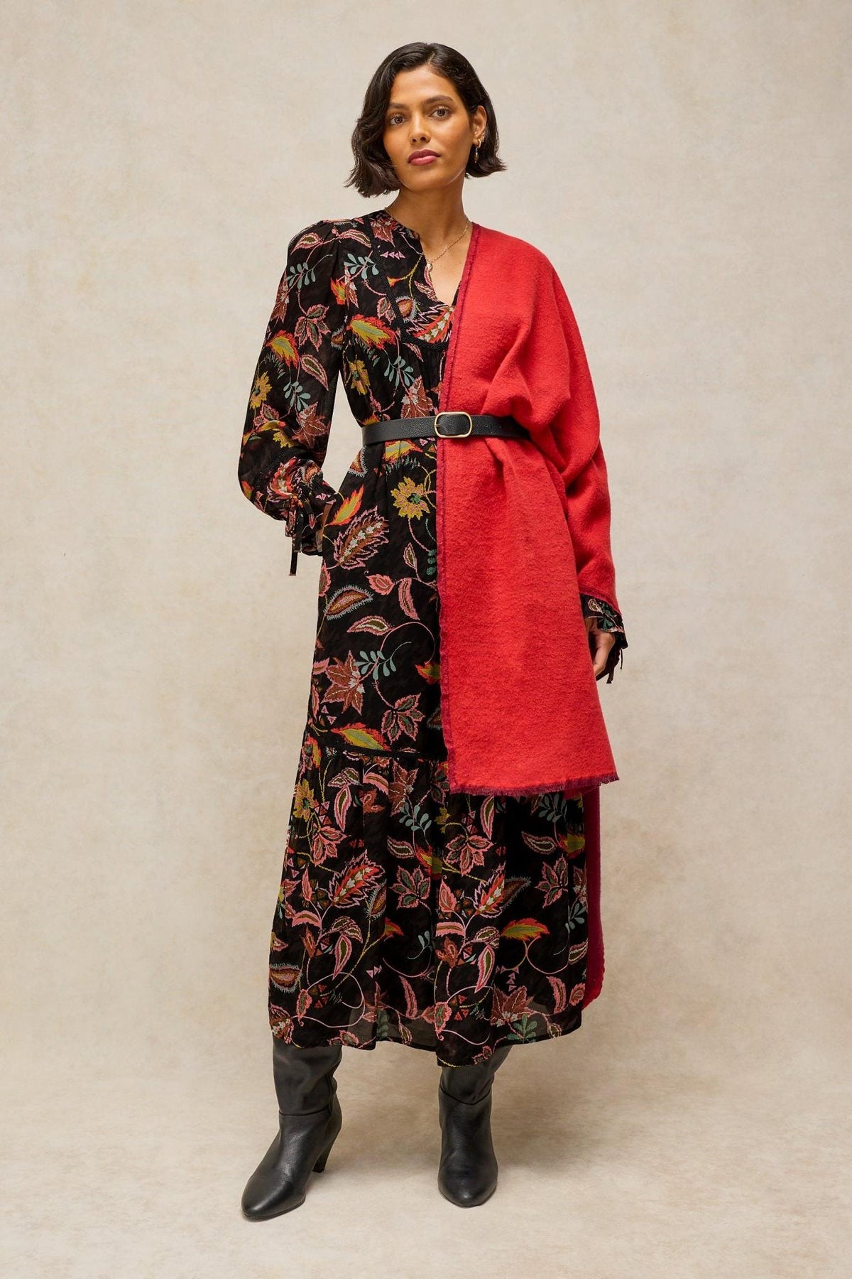 A woman posing in a long black floral viscose dress by White Stuff with a red scarf over her shoulder.