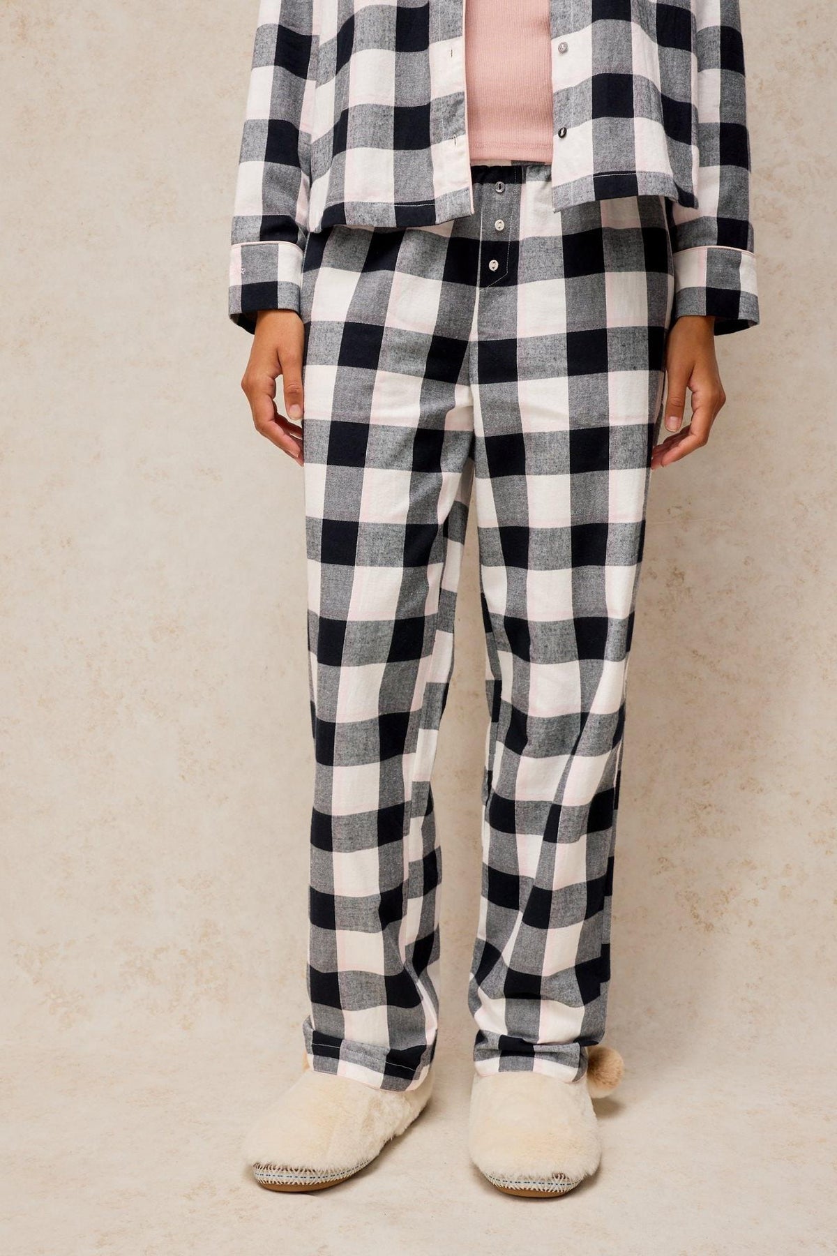 Person wearing White Stuff organic cotton pyjama bottoms with a black check print and fluffy slippers.