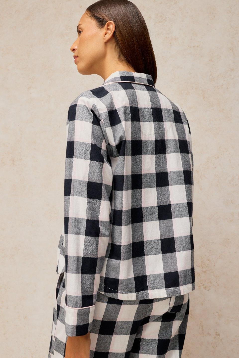 A woman wearing a White Stuff black and white check organic cotton pyjama top against a neutral background.