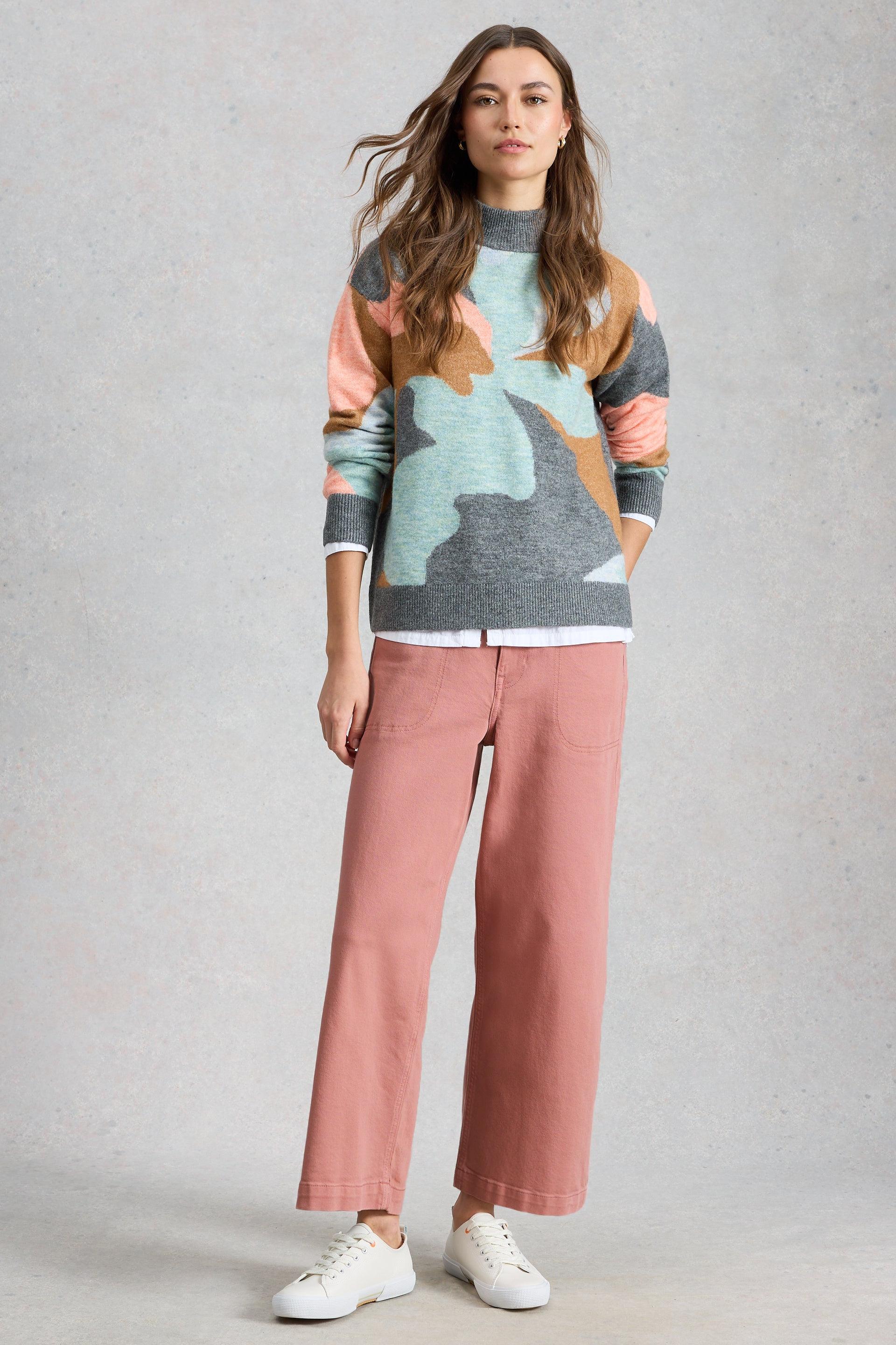 A woman wearing a White Stuff patterned sweater and organic cotton trousers posing against a grey background.
