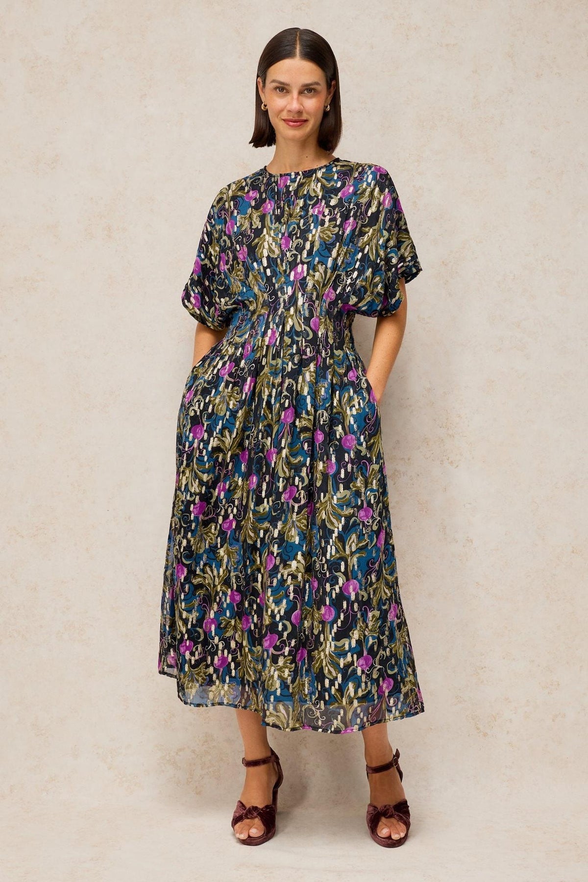 A woman wearing a long, patterned occasion dress with a dark floral print and short sleeves.