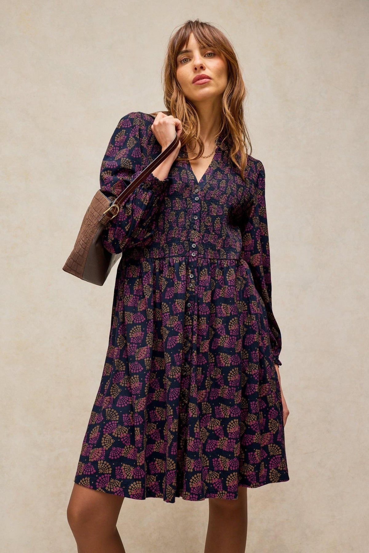 Woman wearing a dark patterned White Stuff knee length everyday dress with a brown handbag.