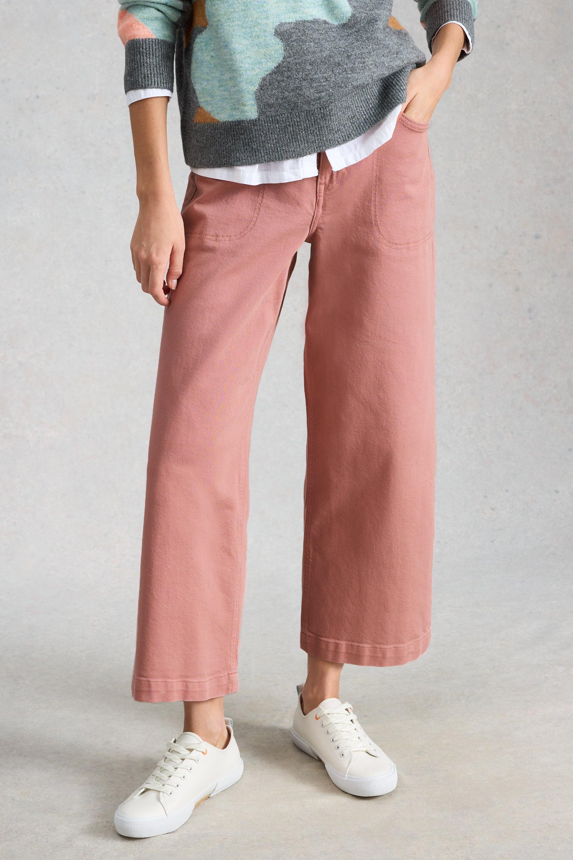 A person wearing pink White Stuff organic cotton trousers, a patterned sweater, and white sneakers.