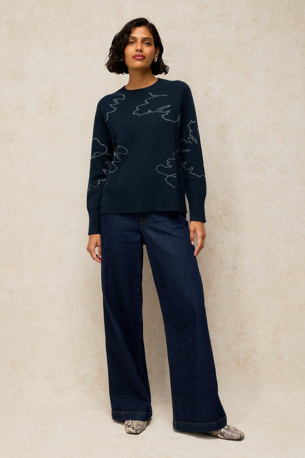 A woman wearing a White Stuff black jumper with sparkly embroidery and wide-leg dark blue jeans.